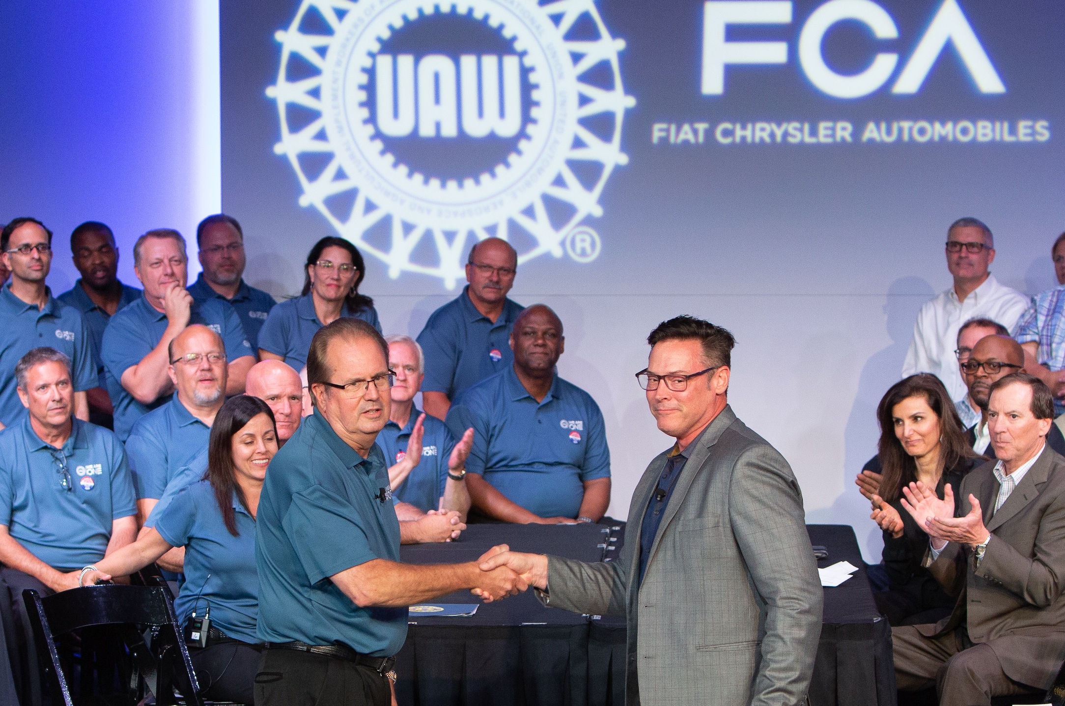 Jones and Stewart are shown shaking hands in front of a negotiating table, with colleagues in the background.