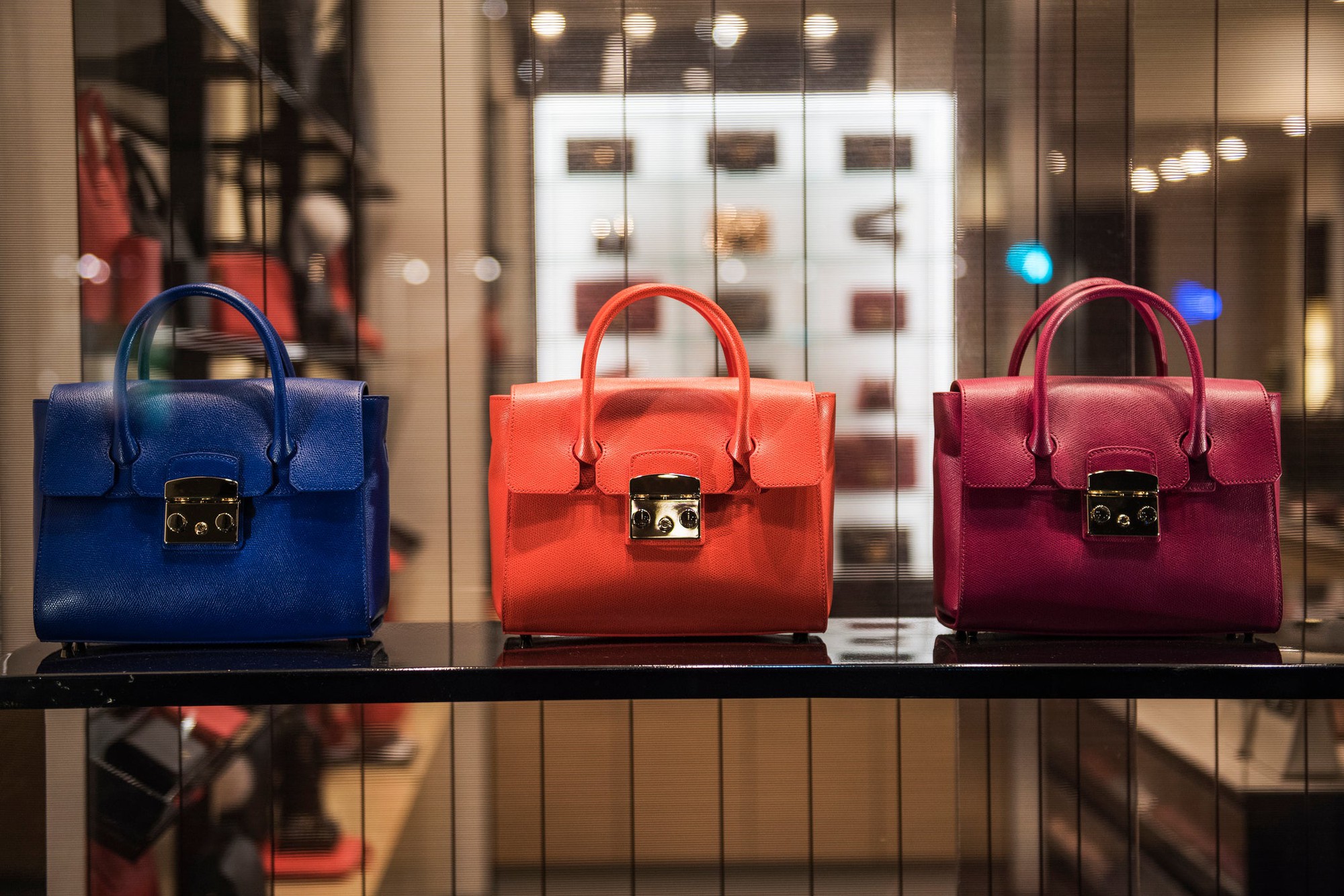 3 leather handbags are shown in a store window.