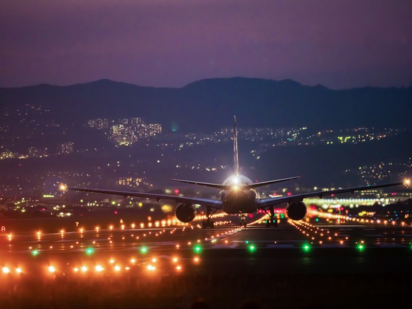 An airplane landing in front of an evening urban landscape.