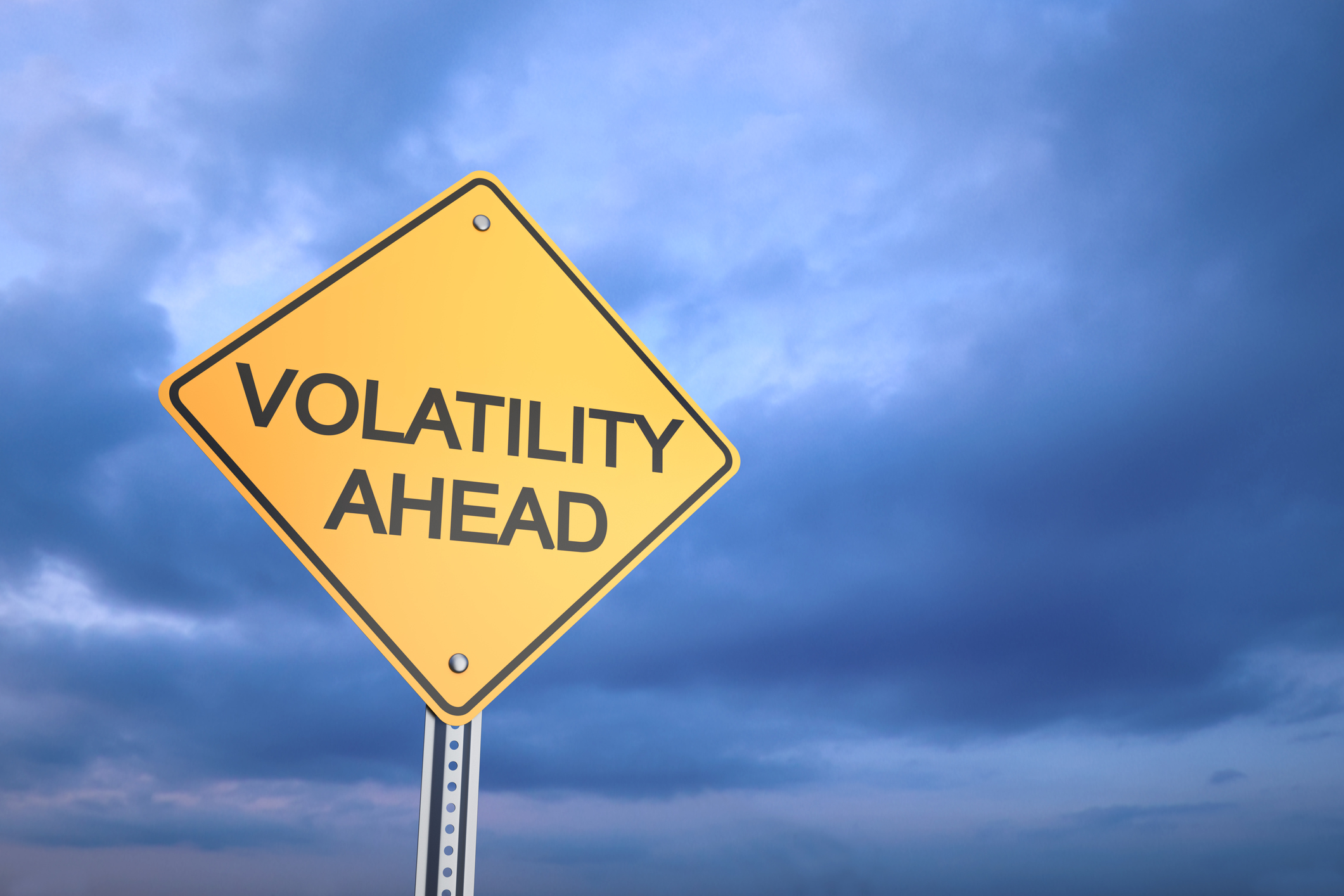 A yellow road sign with the words Volatility Ahead against a dark sky packed with clouds.