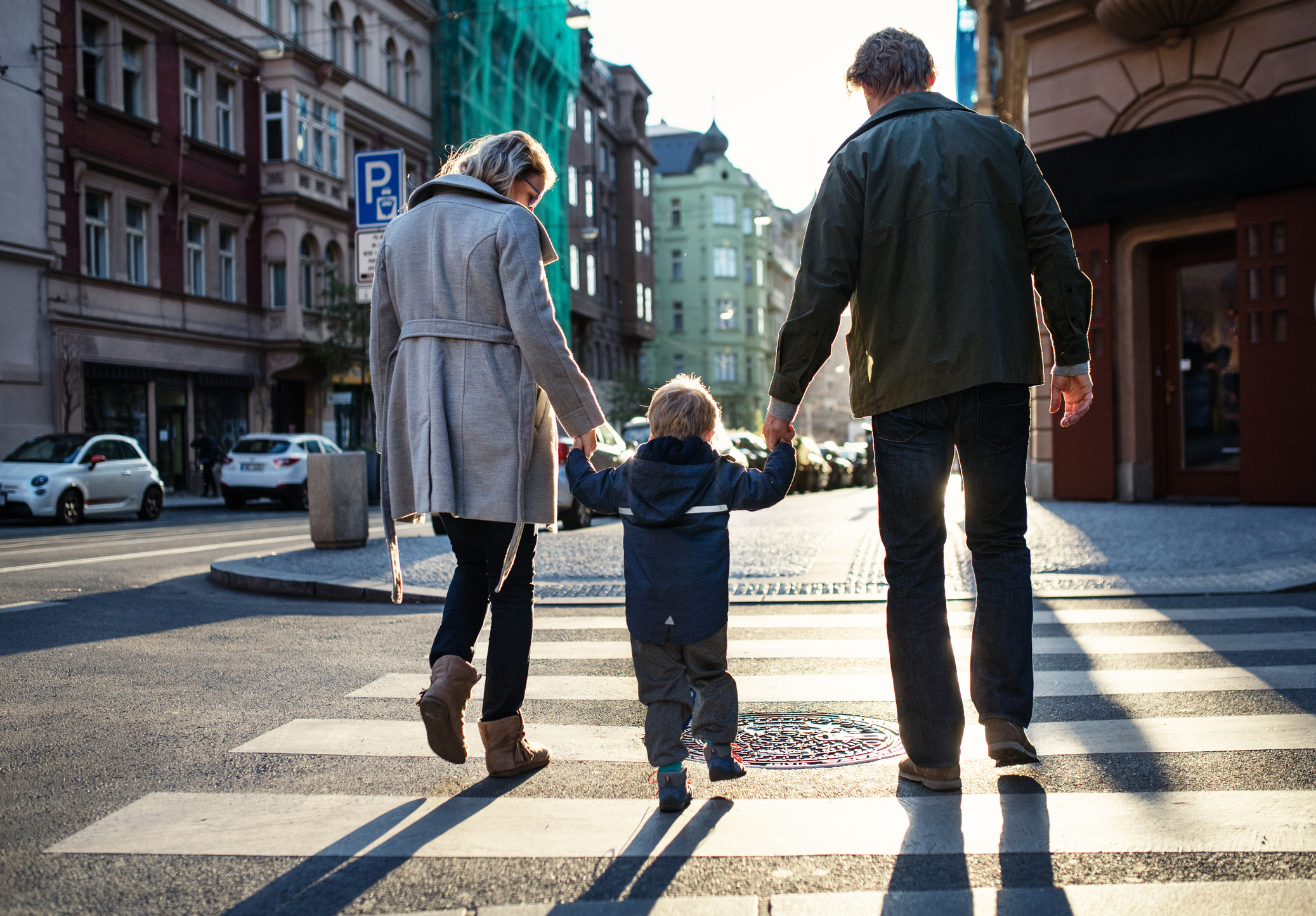 Woman and man holding boy's hands while crossing street
