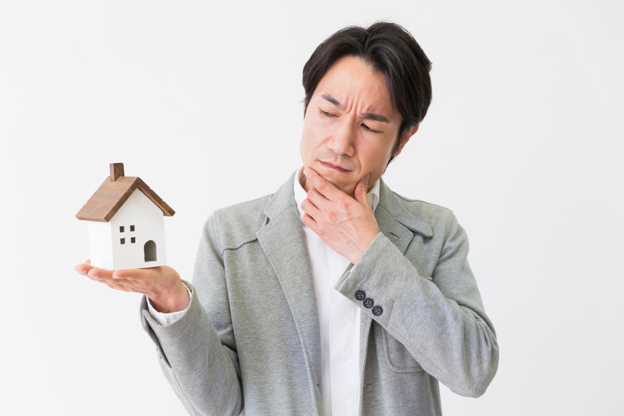 A person looking at a miniature home while holding his chin in a pensive manner.