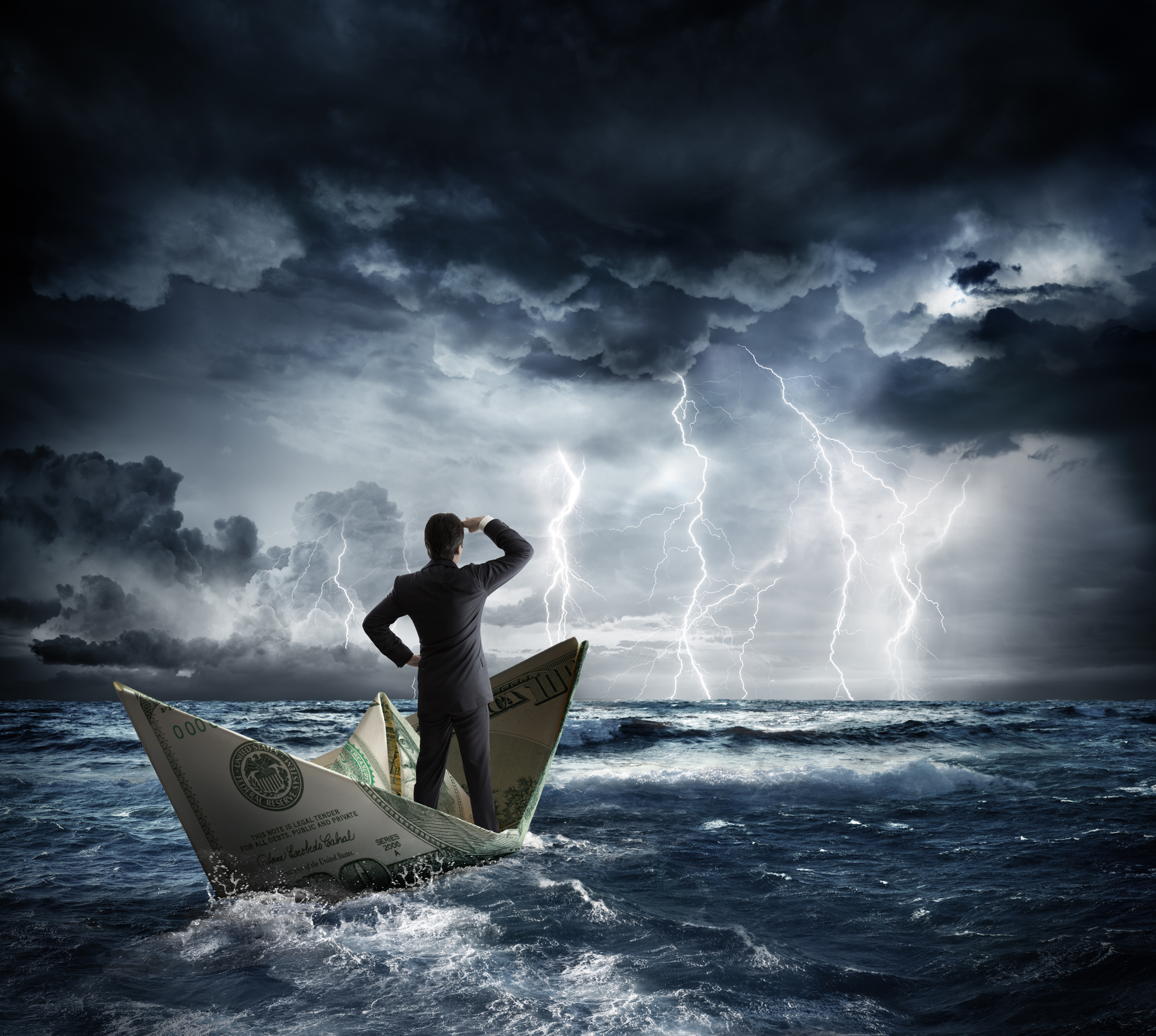 A businessman in a paper money boat staring out at a stormy sea.