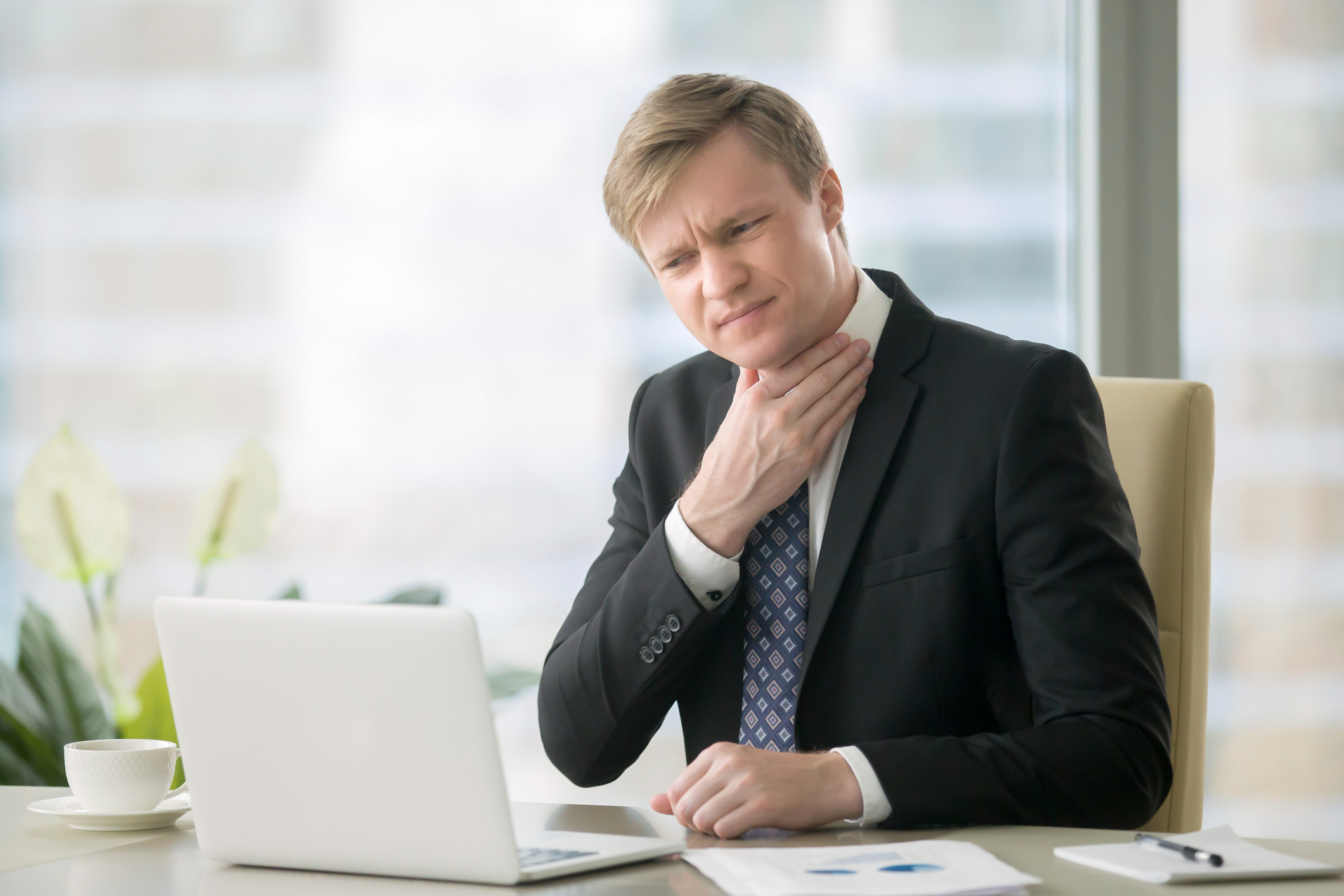 Man in suit at desk touching his neck