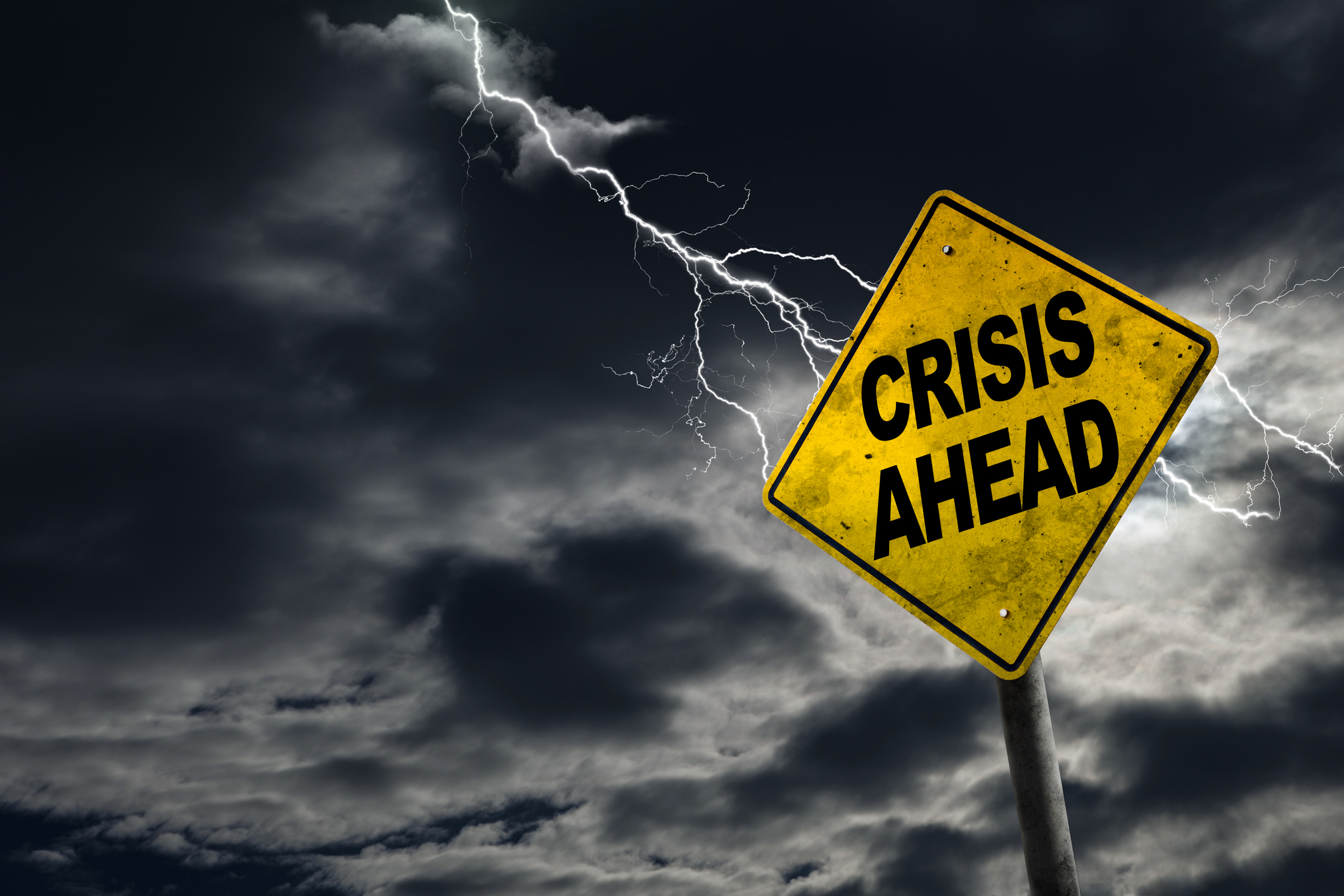 A road sign that says crisis ahead is shown, against a darkened sky with lightning.