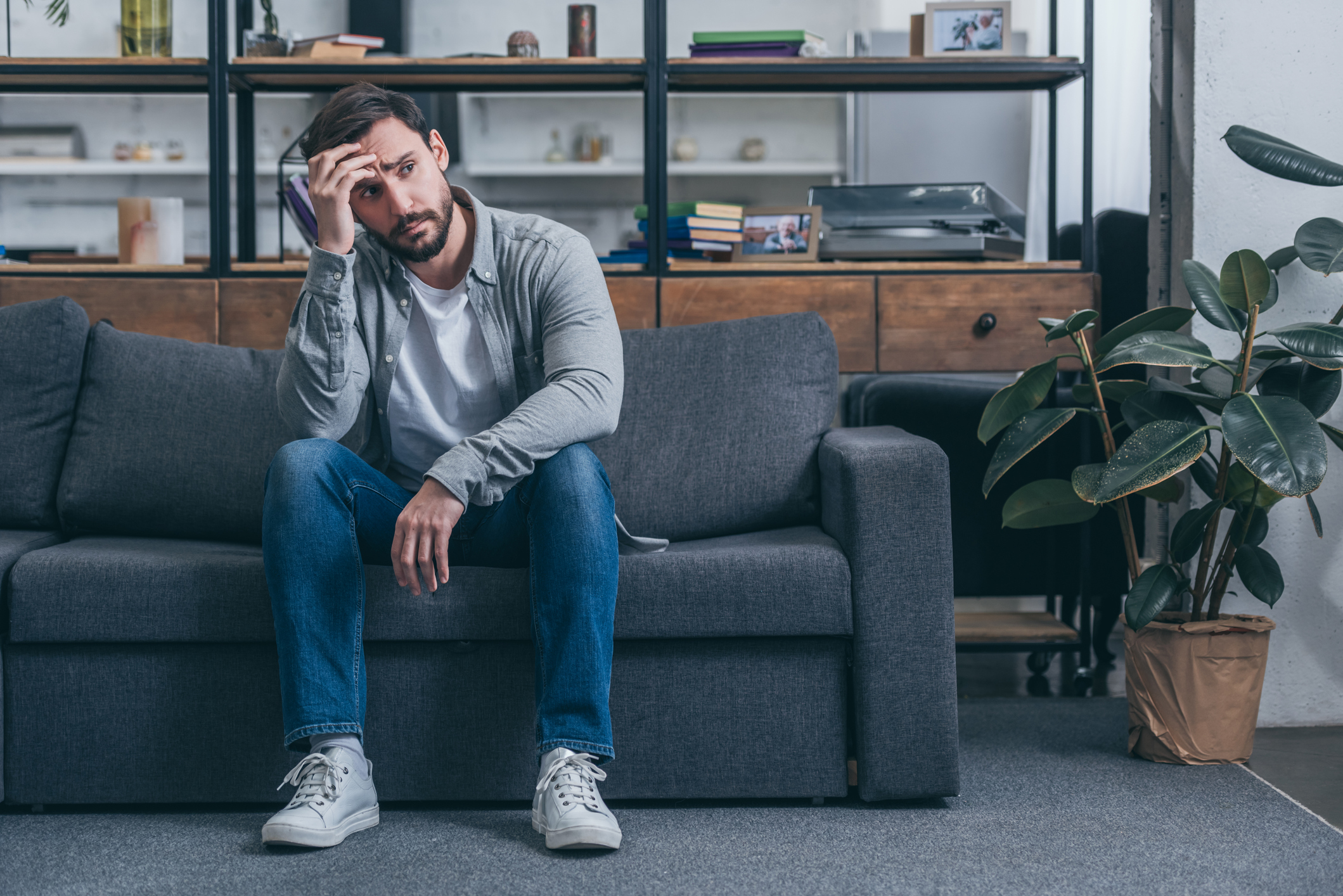 Man with sad expression sitting on couch and holding his head