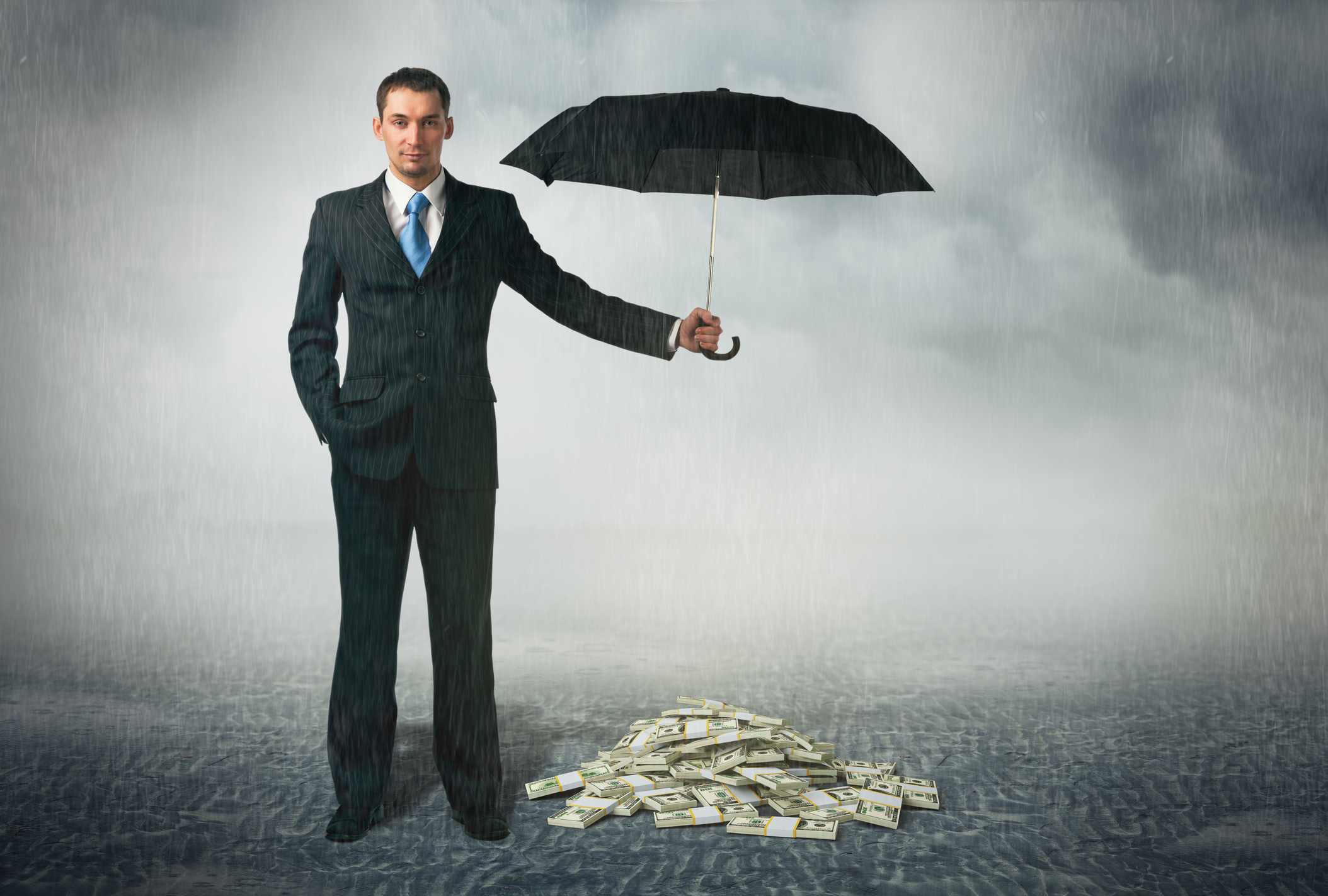 A man in a suit holds an umbrella over a pile of money during a storm.