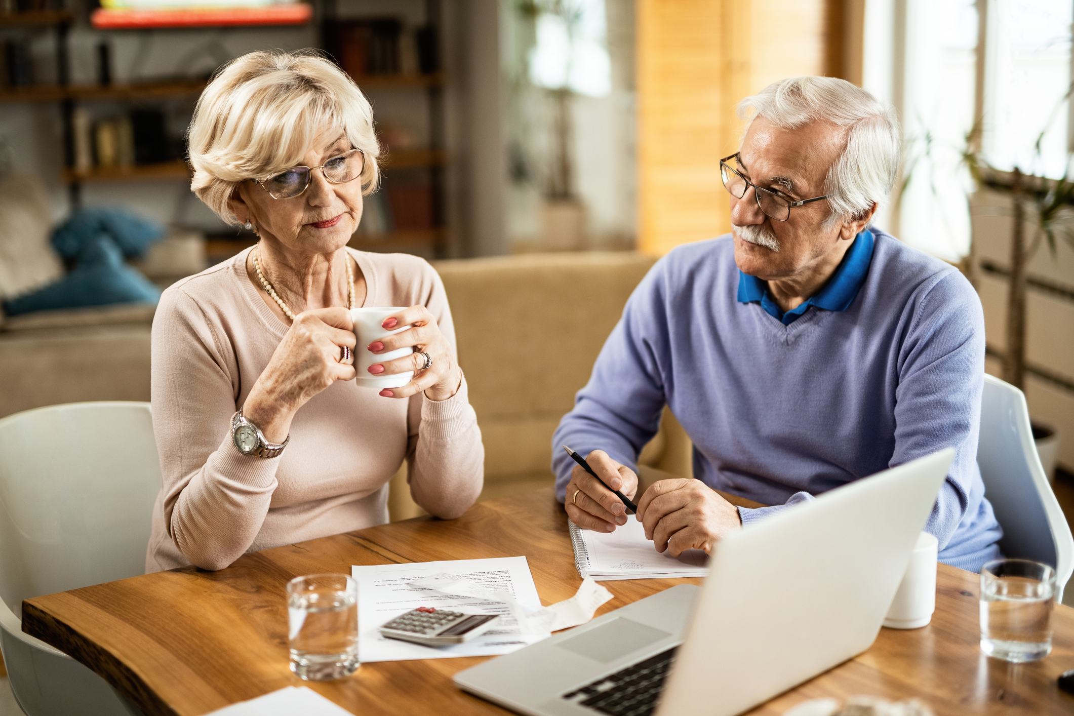 Older man and woman at table with notebook, documents, calculator, and laptop