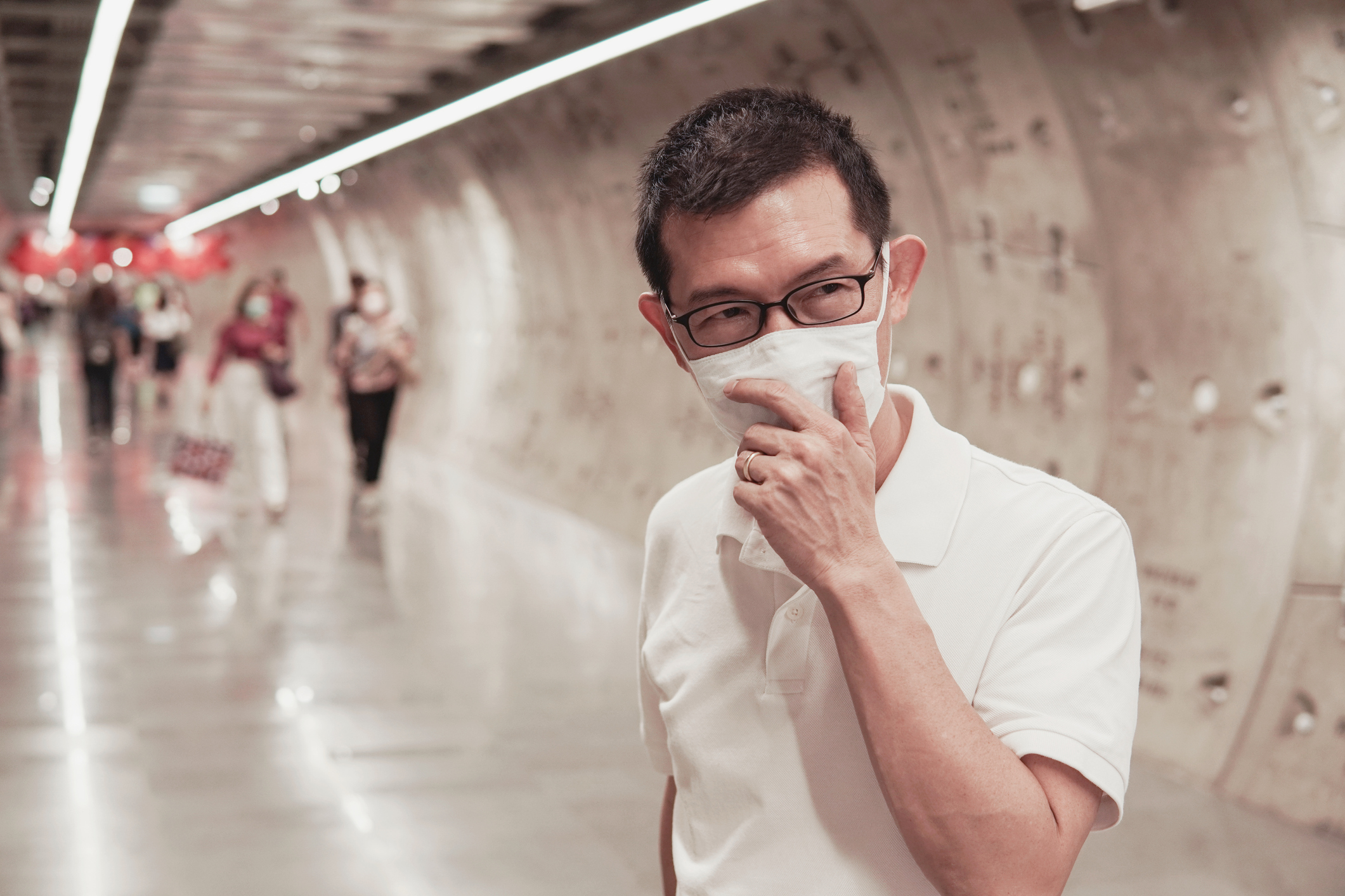 A middle-aged man wearing a medical face mask in a subway station.