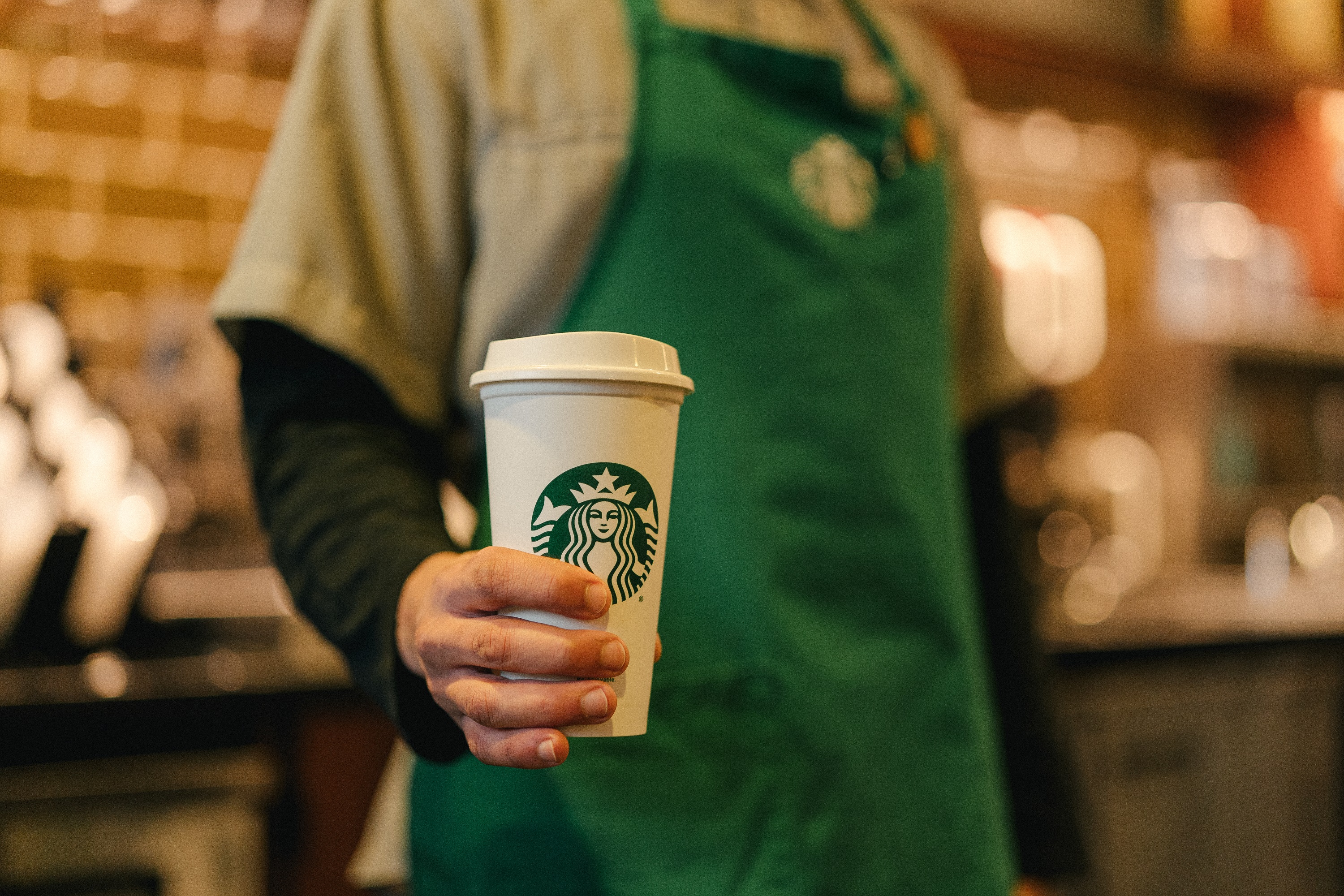 A Starbucks barista holding a paper cup with the Starbucks logo.