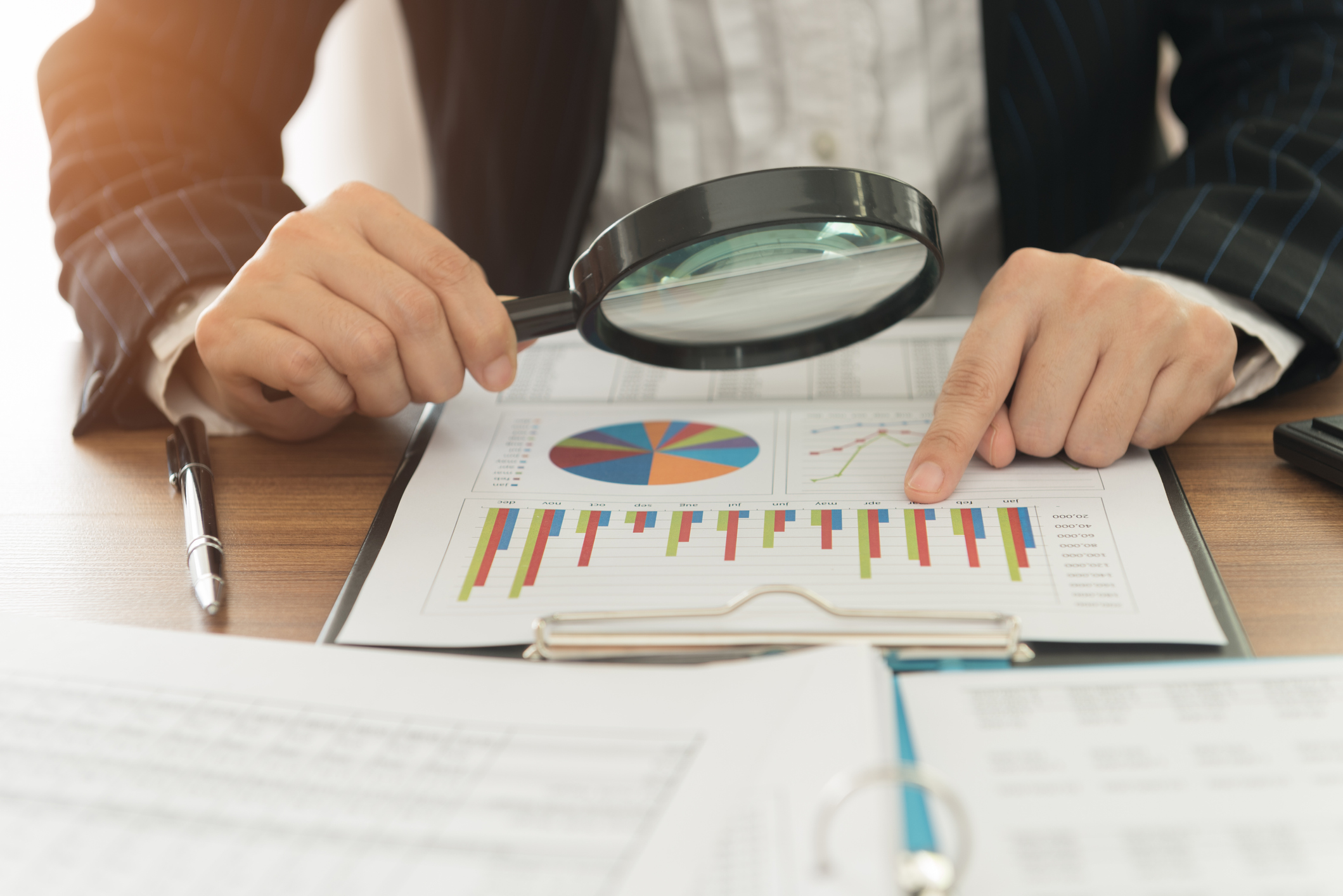 Person looking through a magnifying glass at a business pie chart