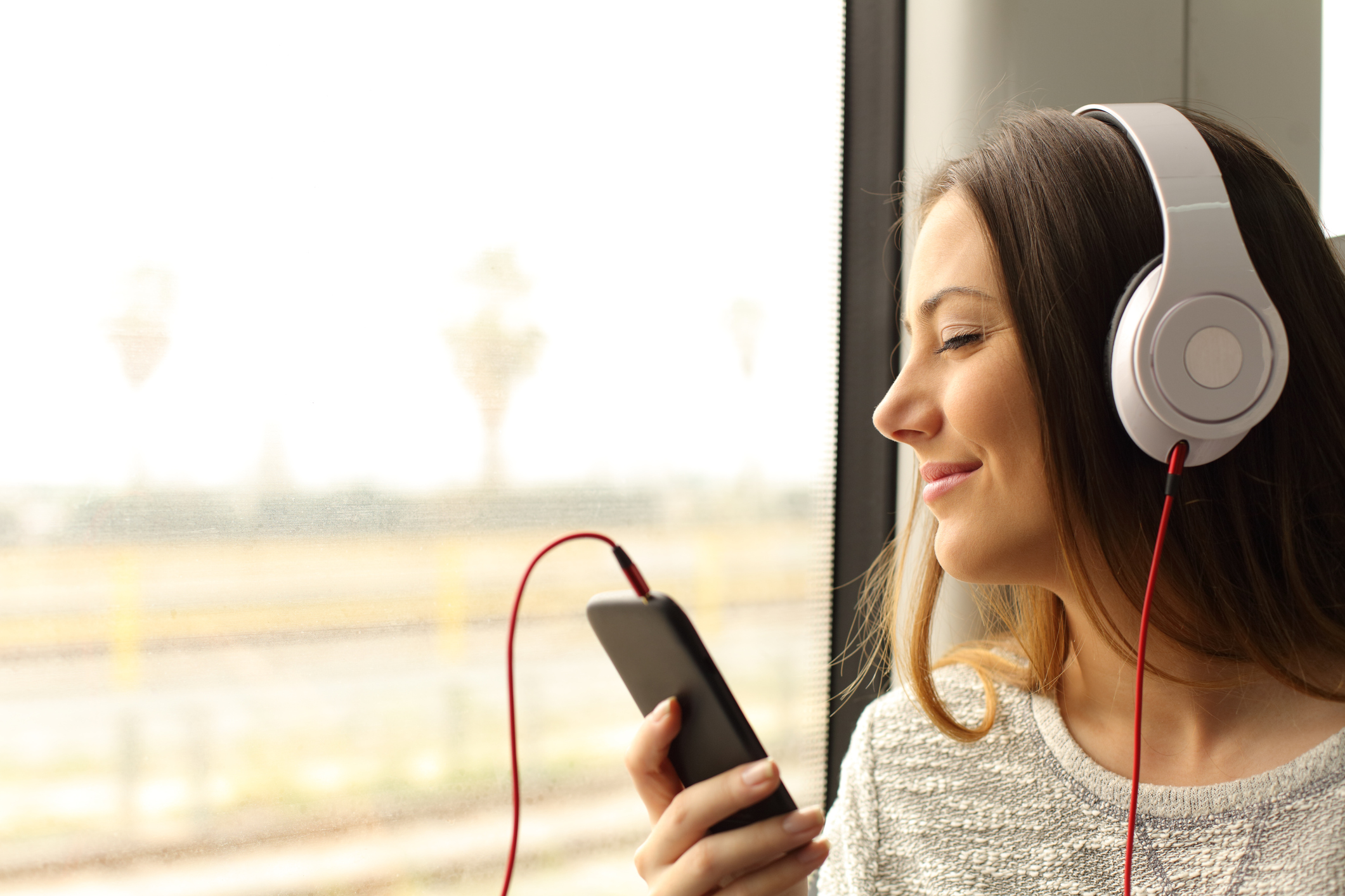 A young woman wearing headphones that are connected to a mobile phone.