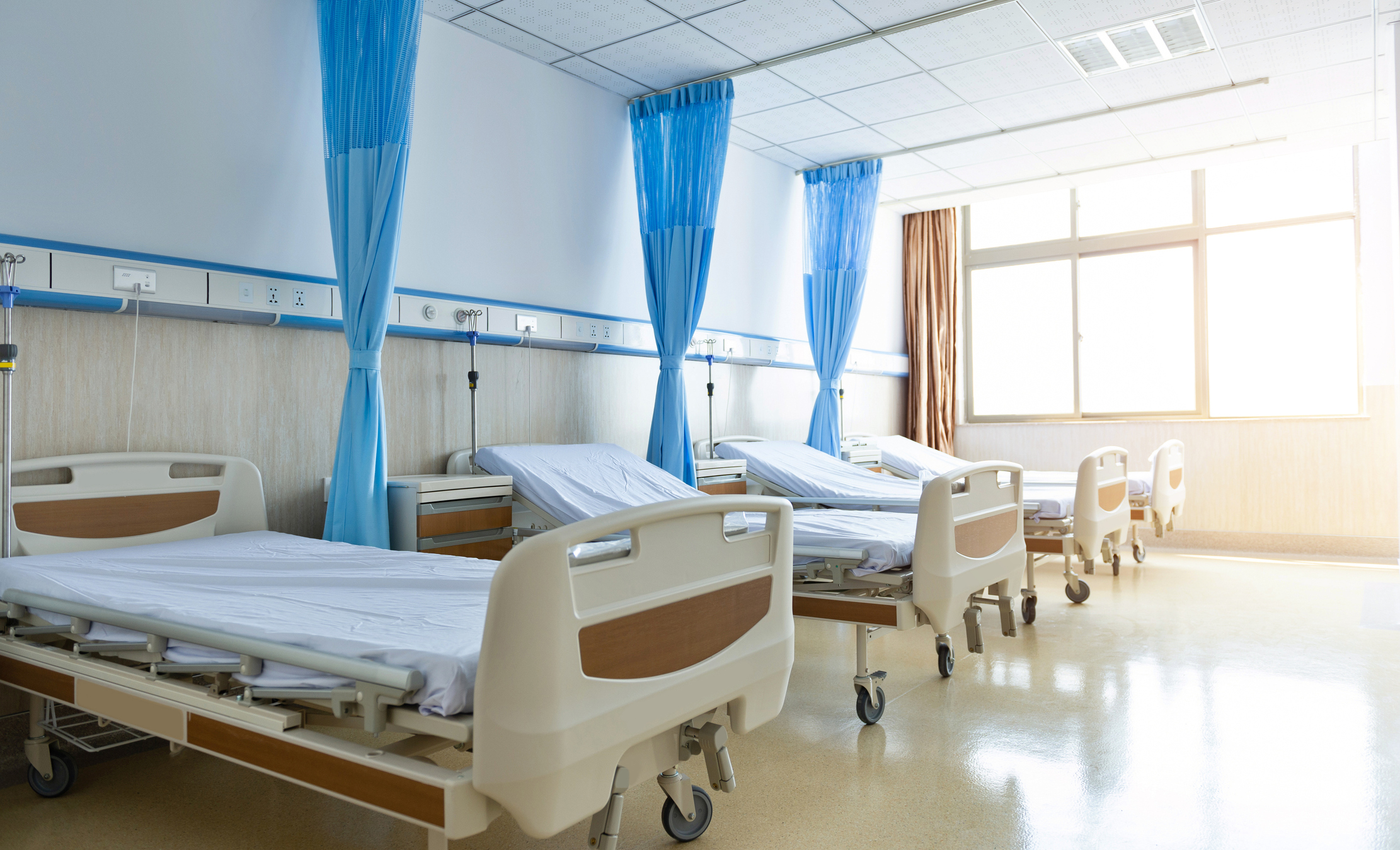 Multiple hospital beds lined up in a hospital room.