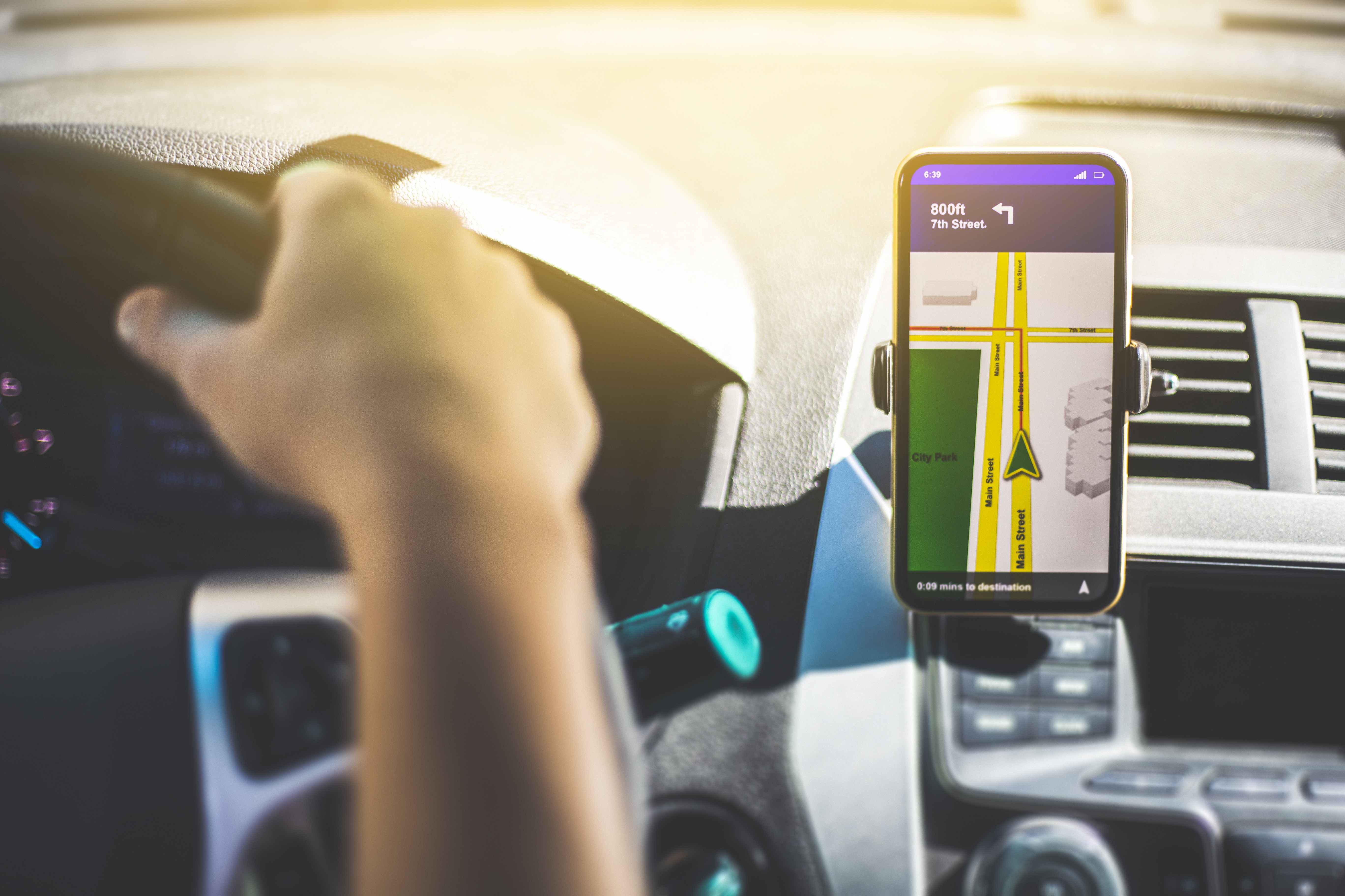 A person driving a car. A smart-device displaying directions is on the dash.