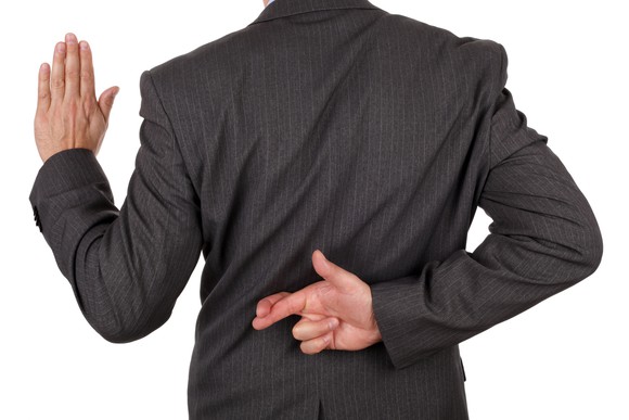 A businessman facing away from the viewer, holding one hand up while crossing his fingers on the other one behind his back.