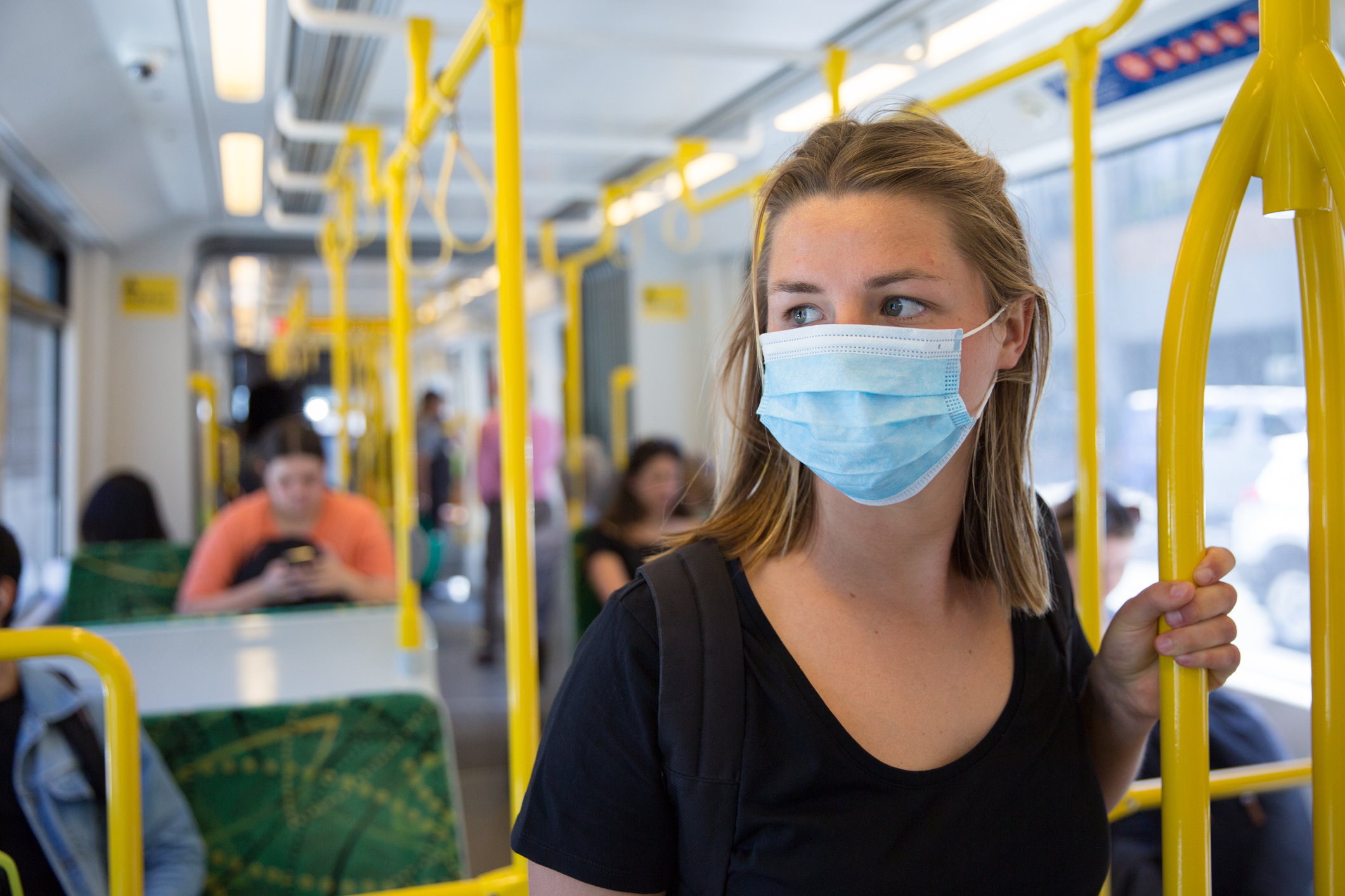 A woman wearing a surgical face mask while on a tram.