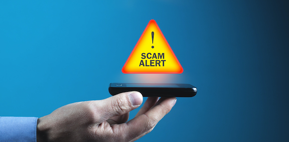 Hand holding phone up, with a Scam Alert caution icon floating above the screen.