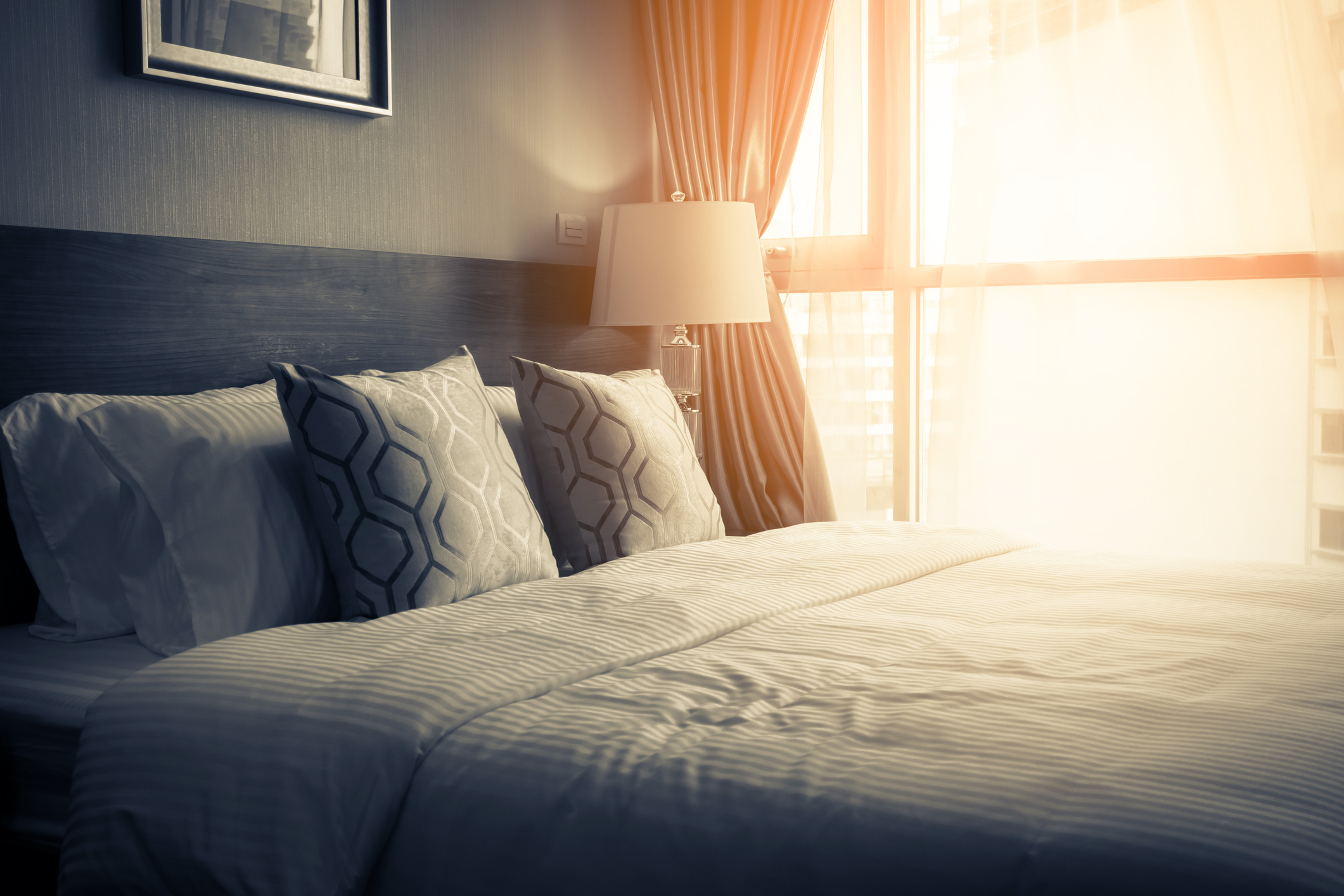 Am empty hotel bed with sunlight coming through the window.