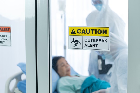 Woman and her doctors behind a caution: outbreak alert sign