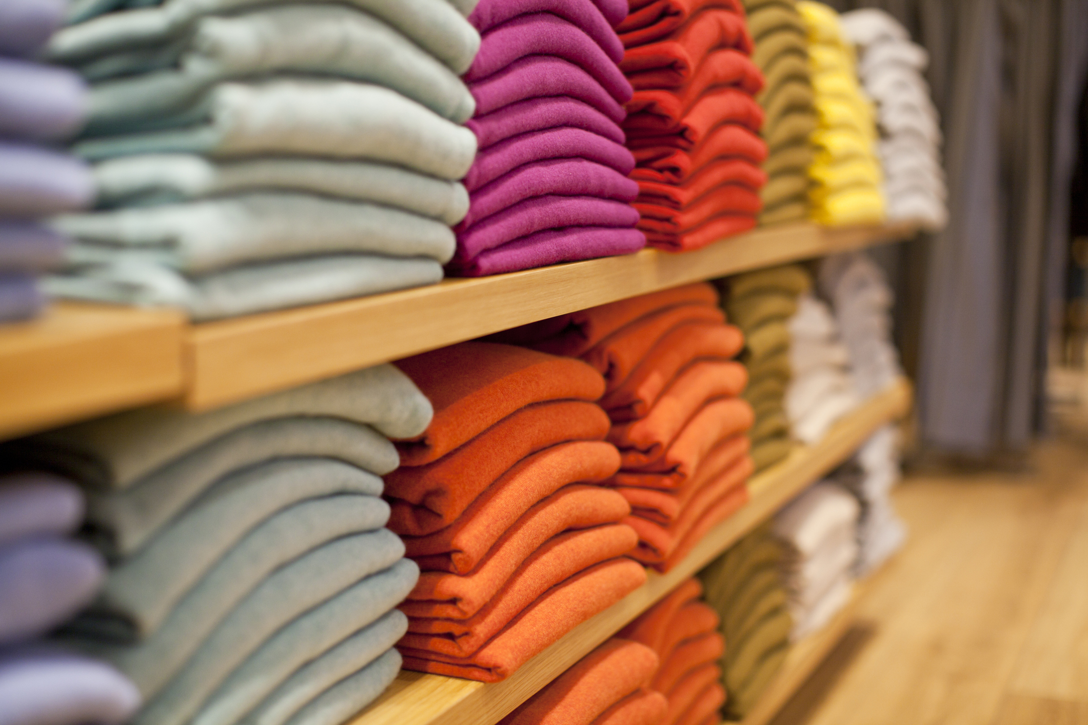 Sweaters in gray, pink, orange and other colors are stacked on store shelves.