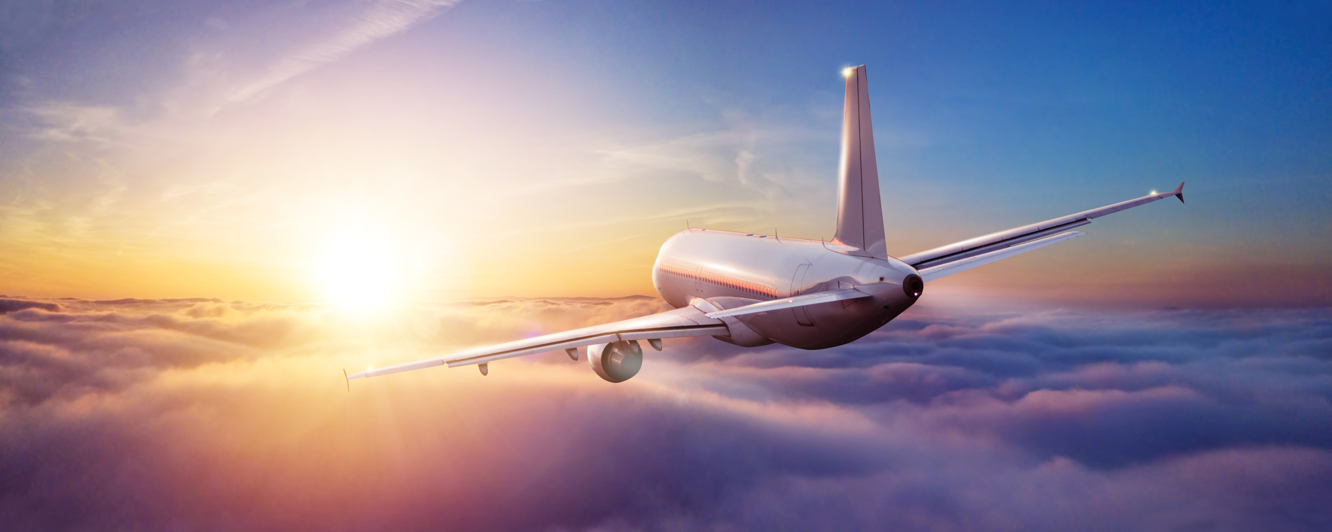 an airplane flies into a setting sun over clouds.