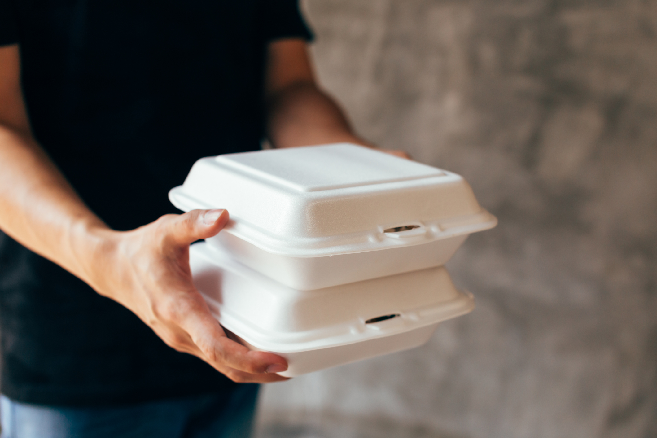 A man in a black t-shirt carries two Styrofoam takeout boxes.