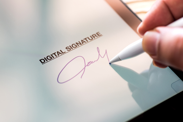 Person's hand signing a tablet with a digital pen,