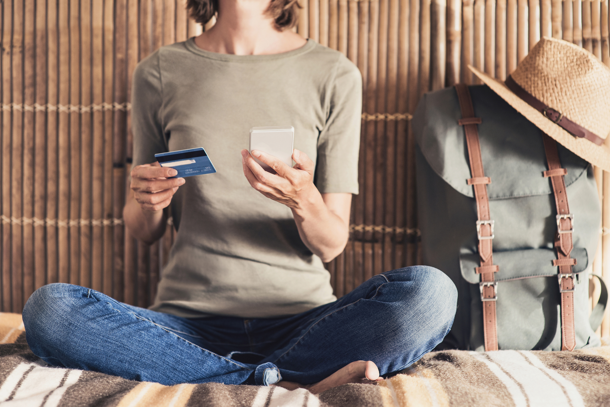 Woman sitting on a bed while using her credit card to make a purchase on her phone.