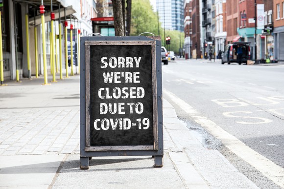 A foldable sign in front of a store that reads, Sorry We're Closed Due to COVID-19.