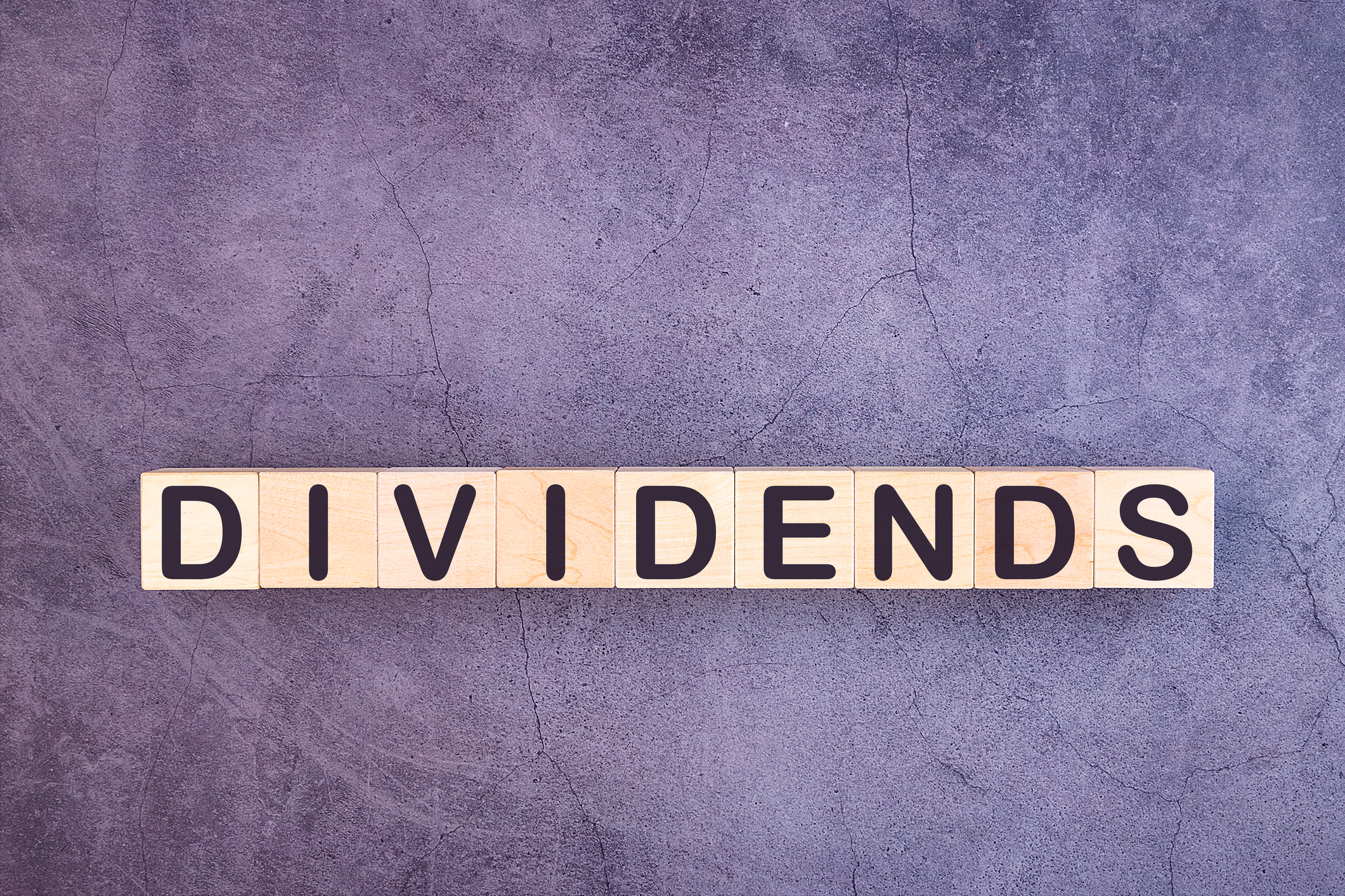 The word "dividends" spelled out on wooden blocks against a gray background.