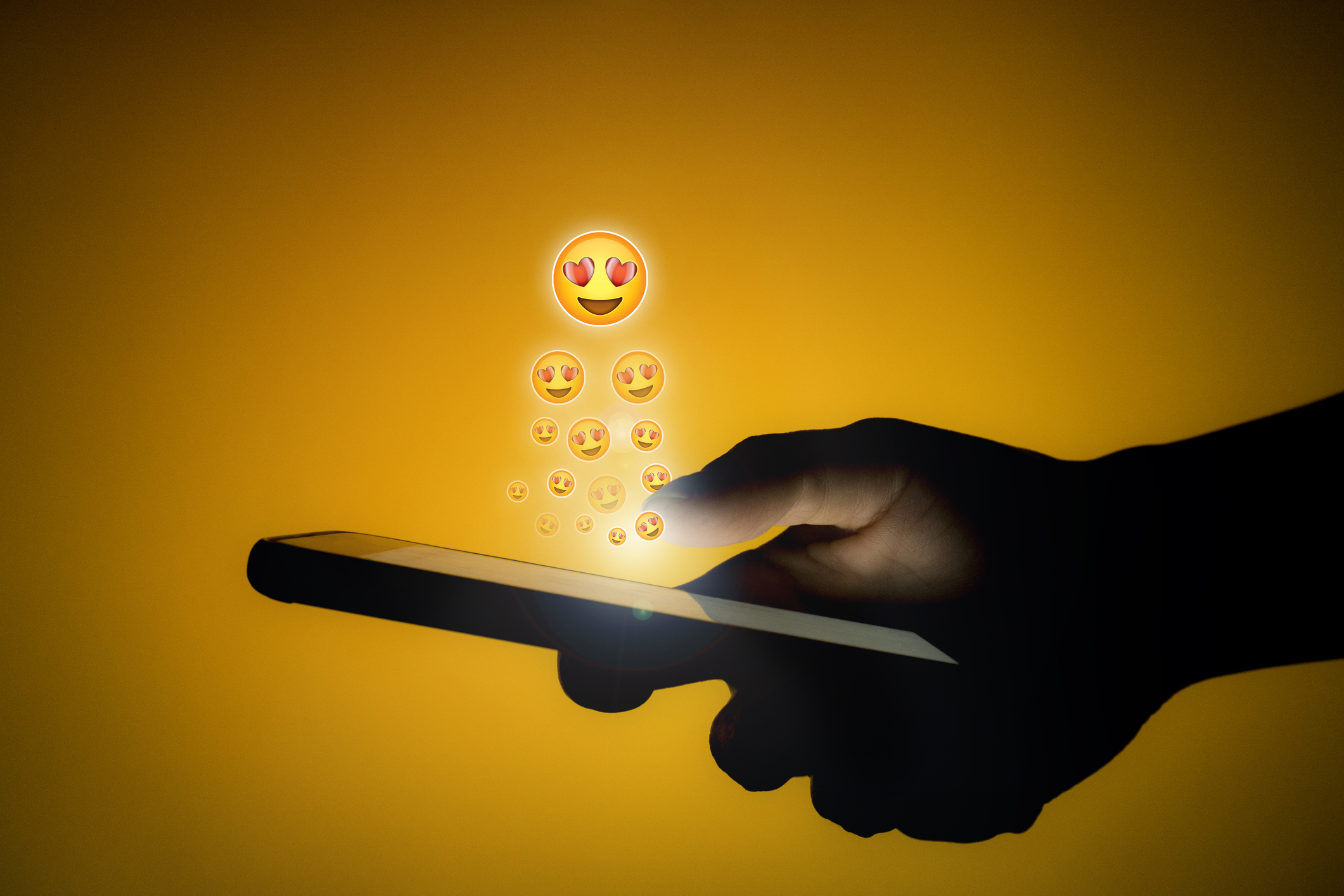 Emojis with heart-shaped eyes rise out a smartphone.