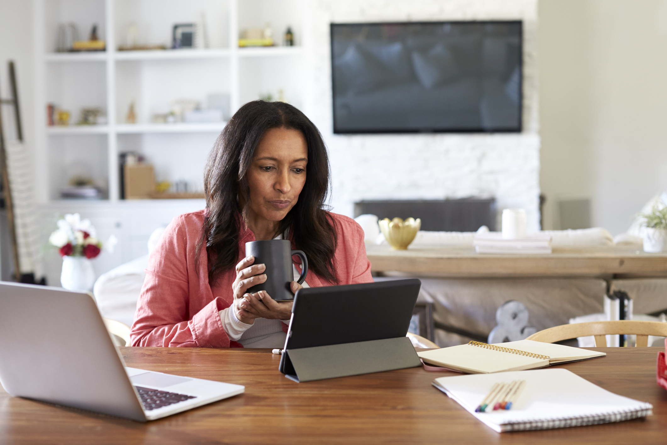 Woman looking at tablet; behind her is a living room with a wall unit and TV