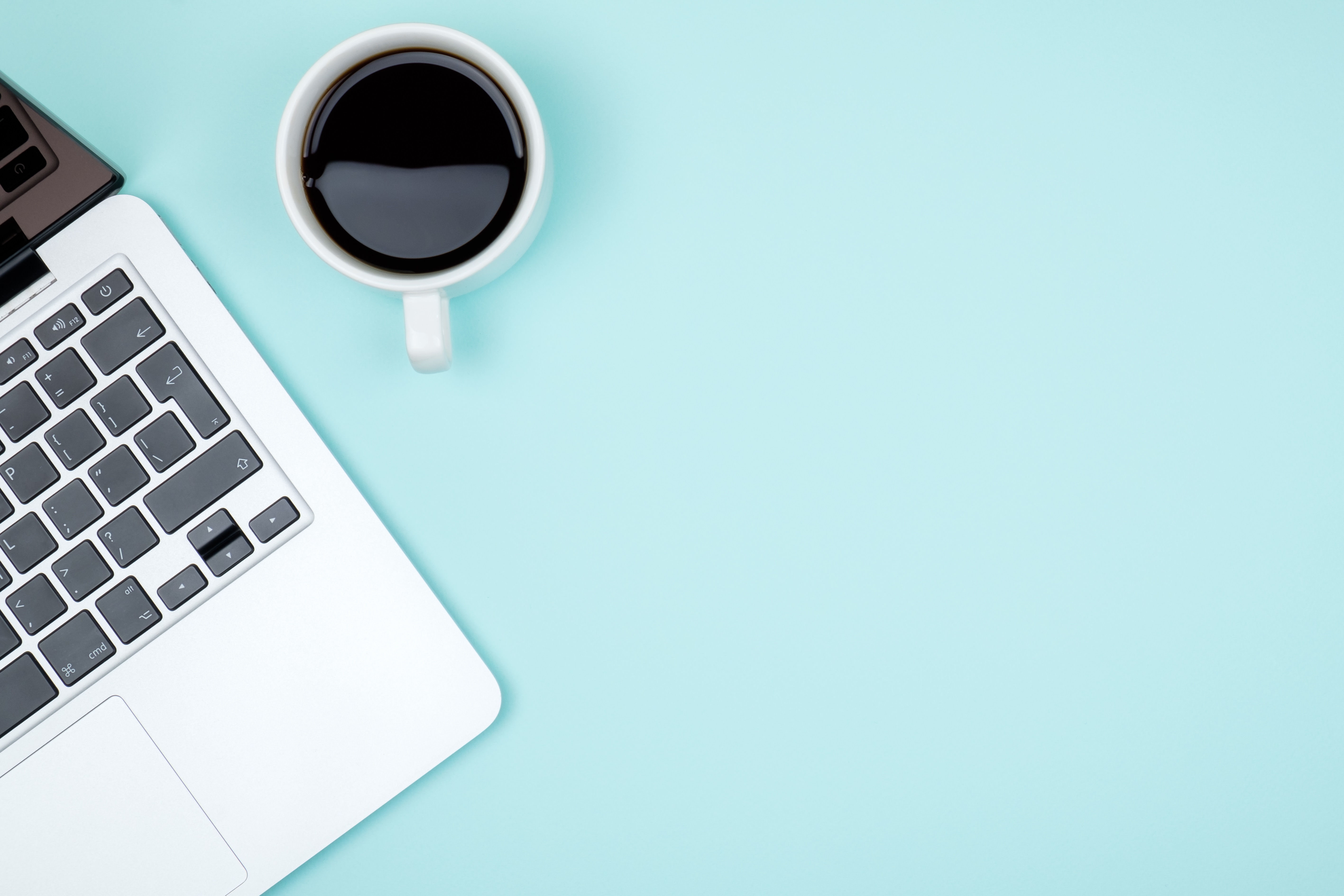 Laptop and a cup of coffee sitting on a table with a blue background.