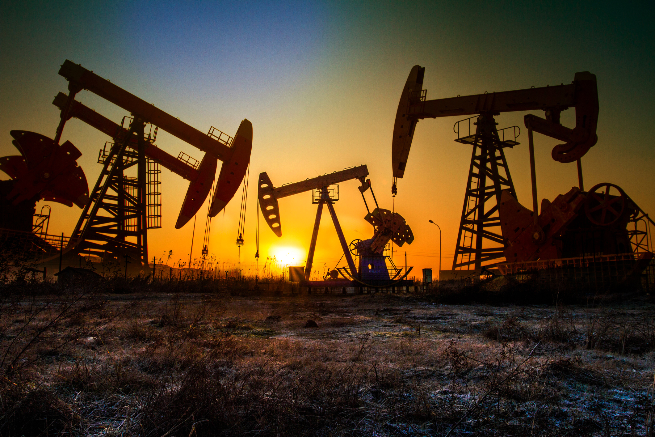 Oil wells in the shadows with a setting sun in the background.