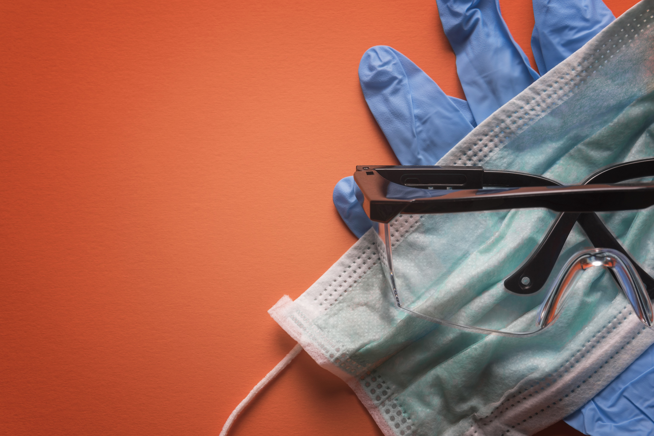 Gloves, face mask, and safety goggles on an orange background.