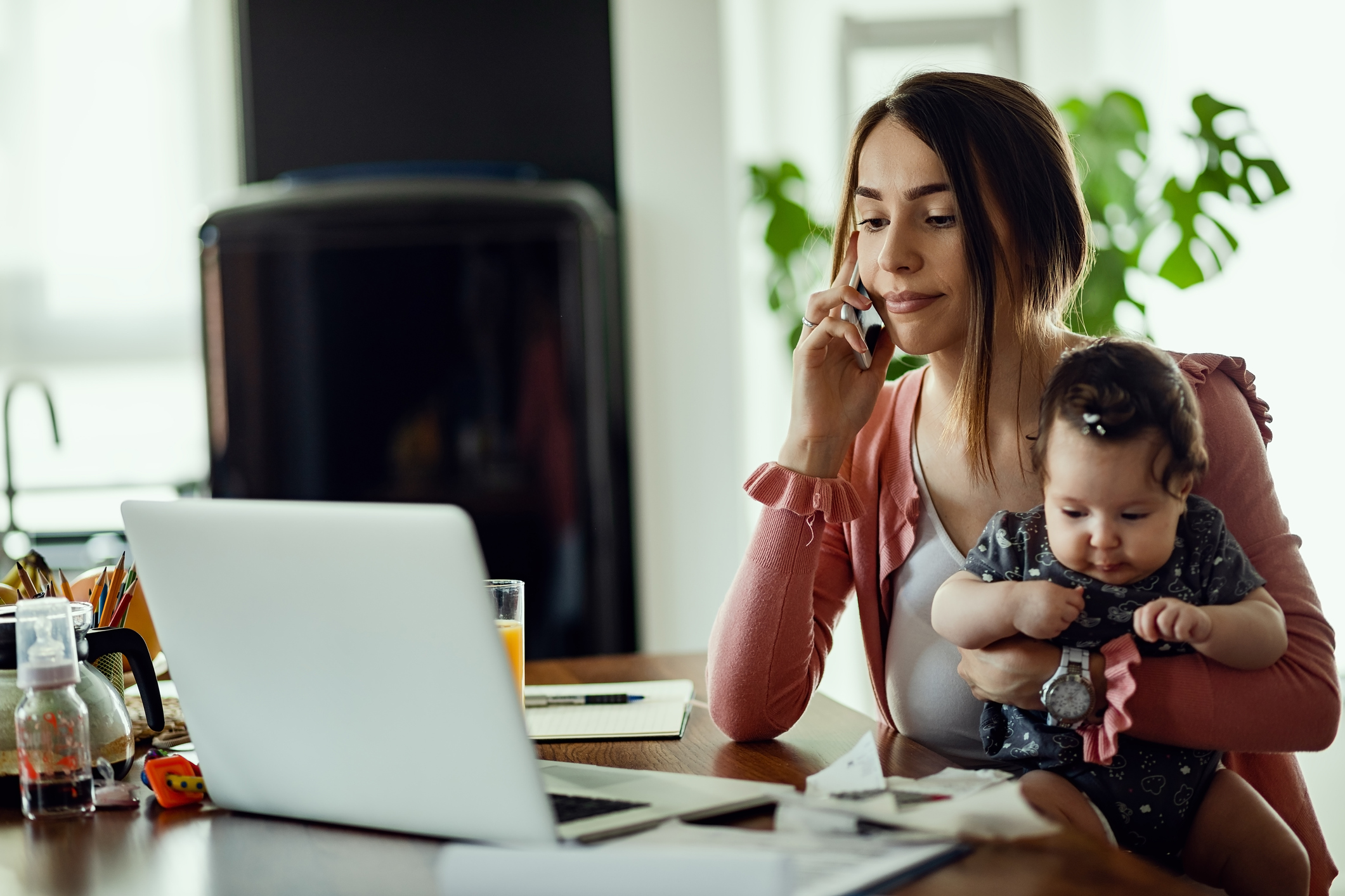 Young mother talking on the phone while using laptop in home office.