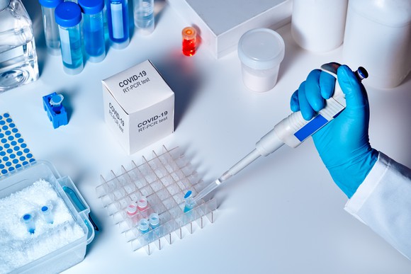 A person's hand wearing a glove and holding a syringe as the person tests a COVID-19 sample.