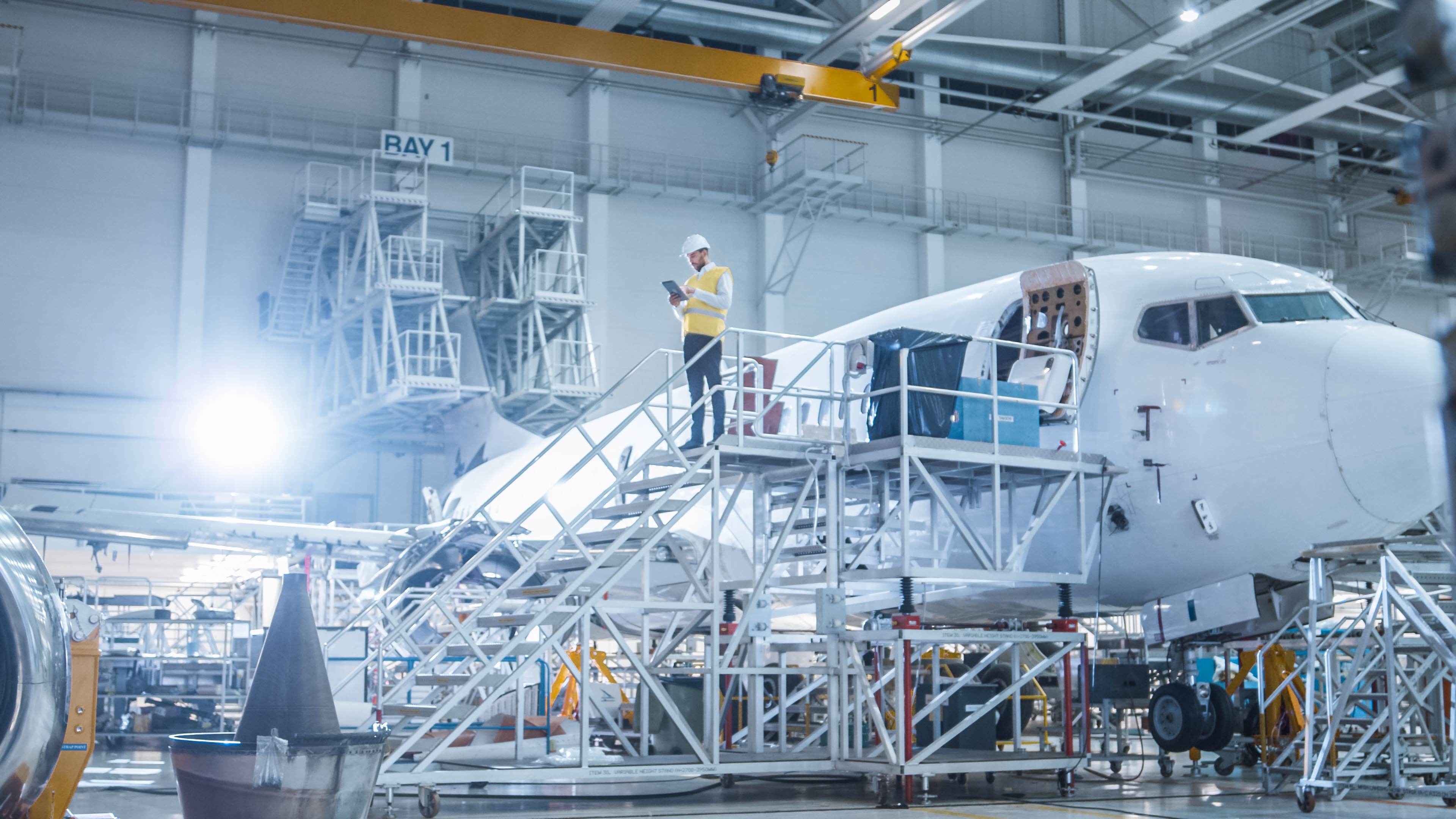 Worker standing on platform next to fuselage at airplane manufacturing plant