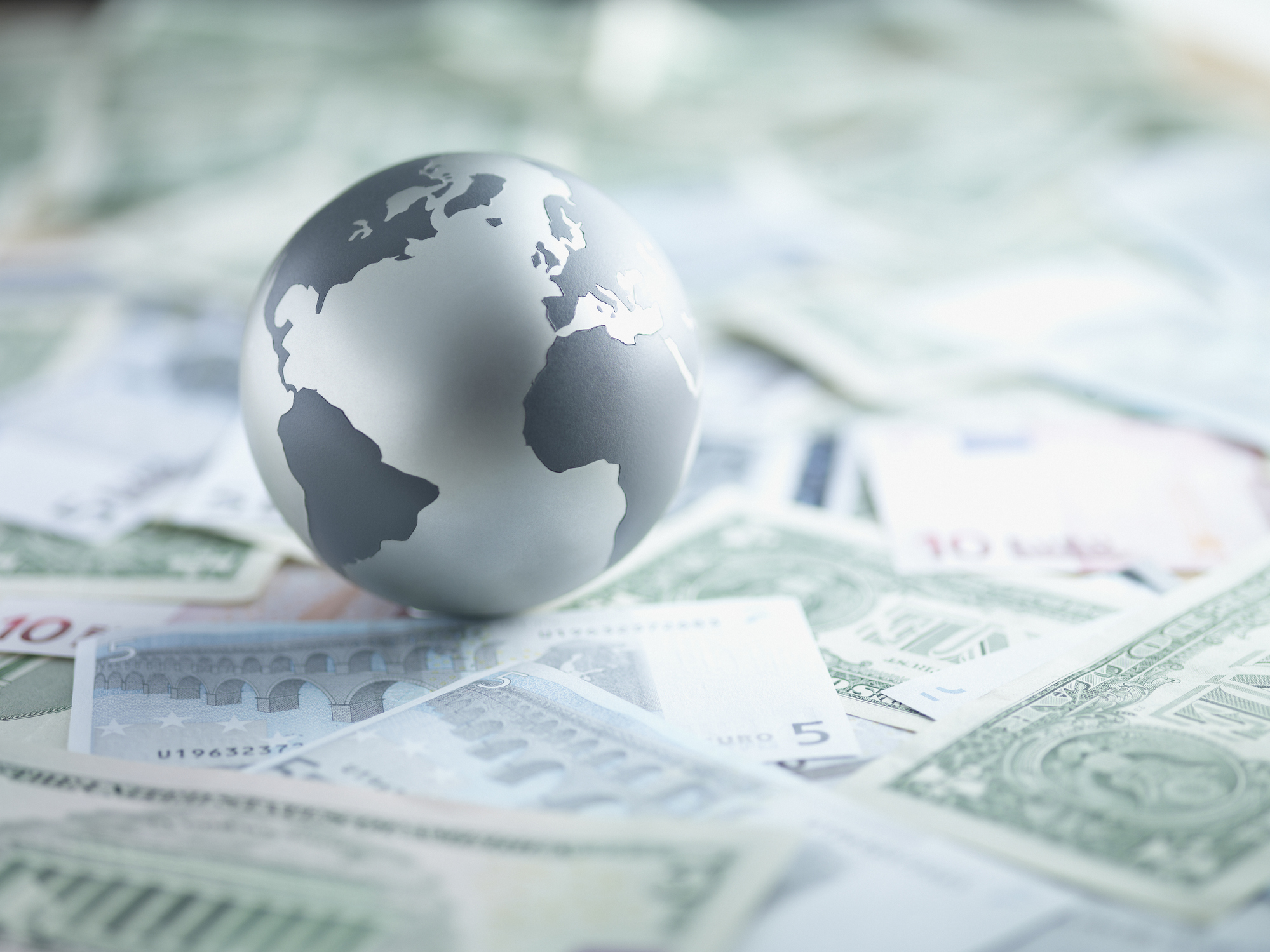 A globe sitting on top several foreign currencies.