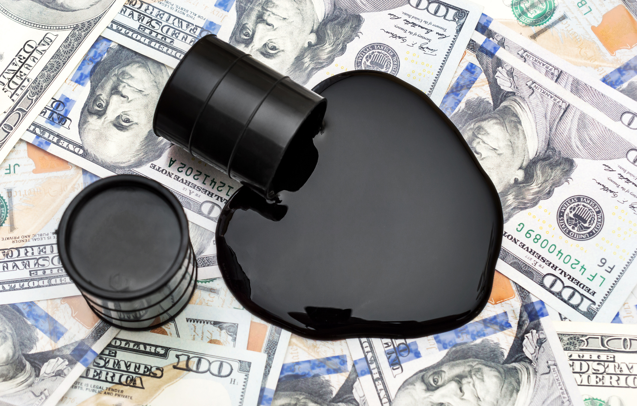 A barrel spilling oil on $100 bills.