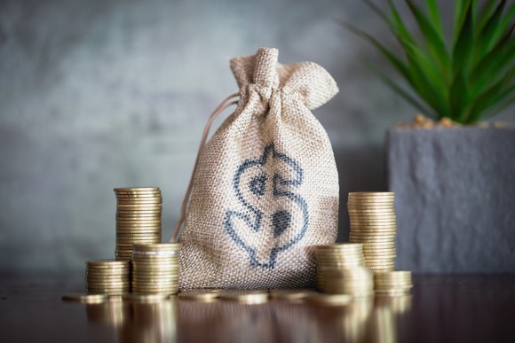 A bag with a dollar sign on it and several stacks of coins