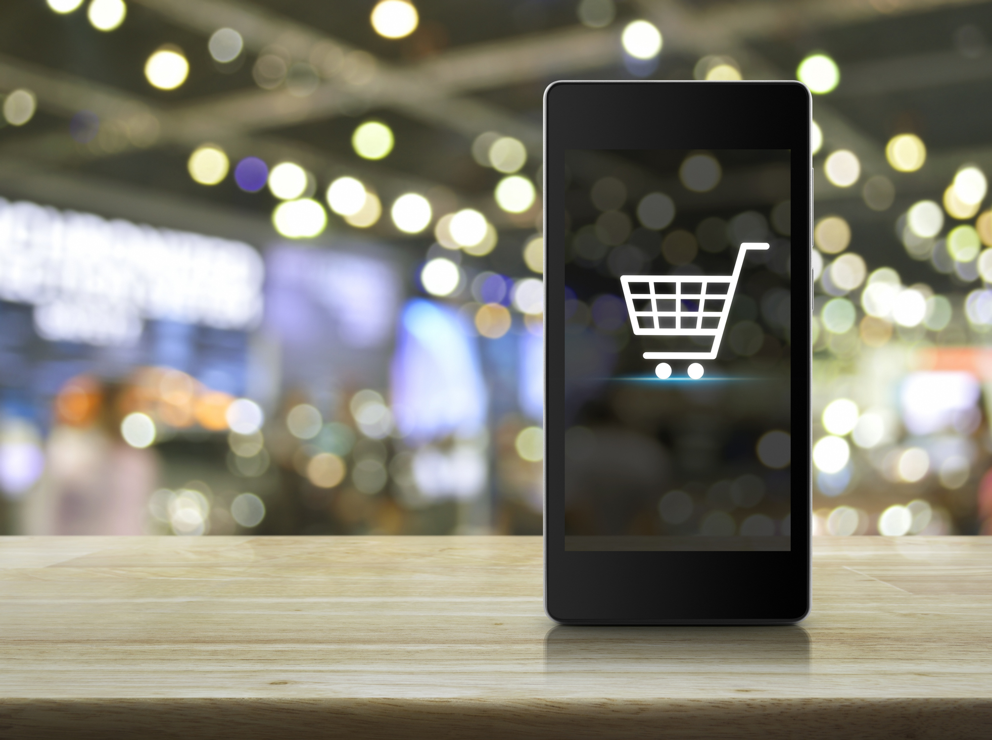 Shopping cart Icon on smart phone screen over a blurred out mall.