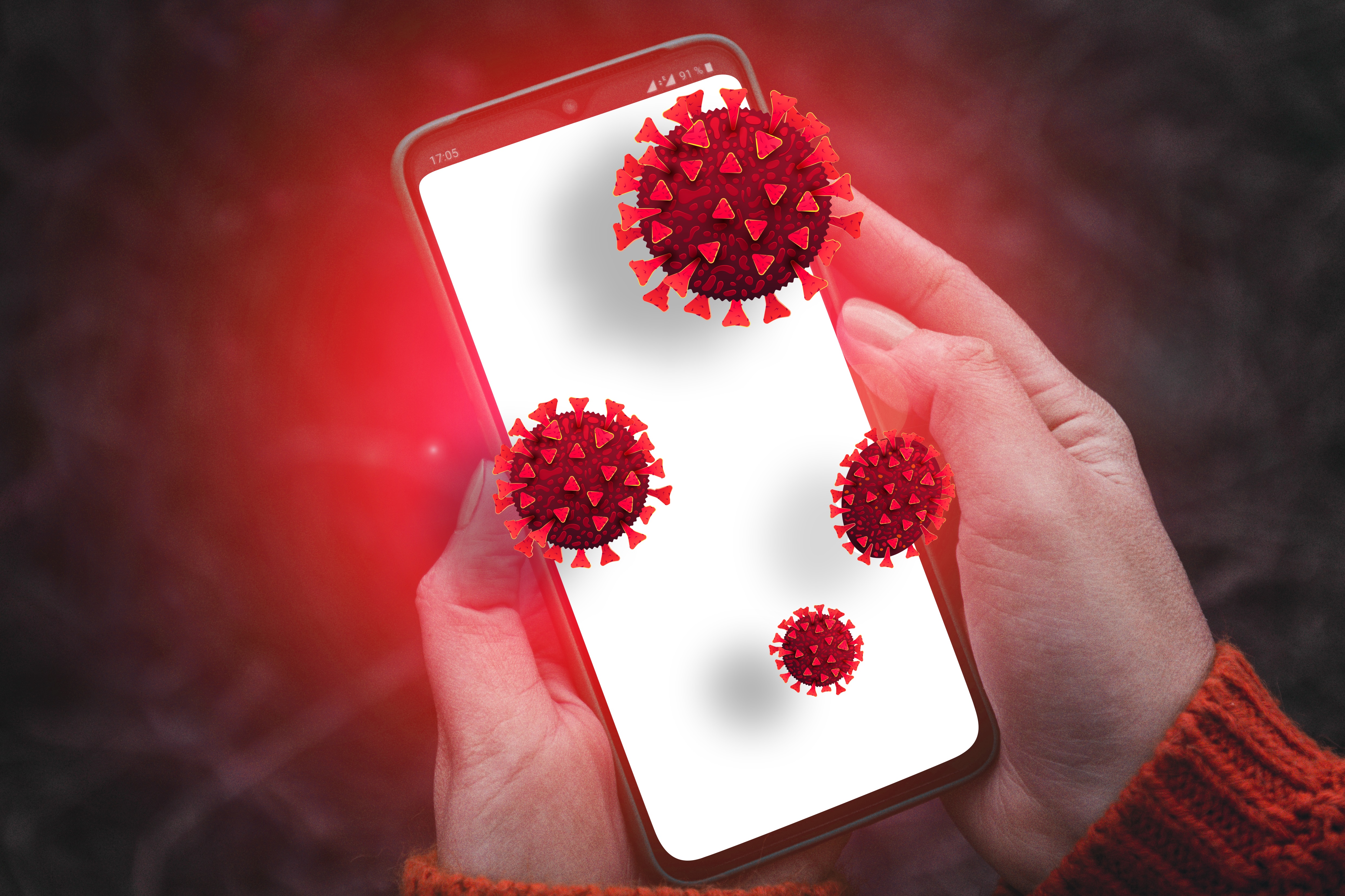 A person holding a white smartphone with red coronavirus cells on it.