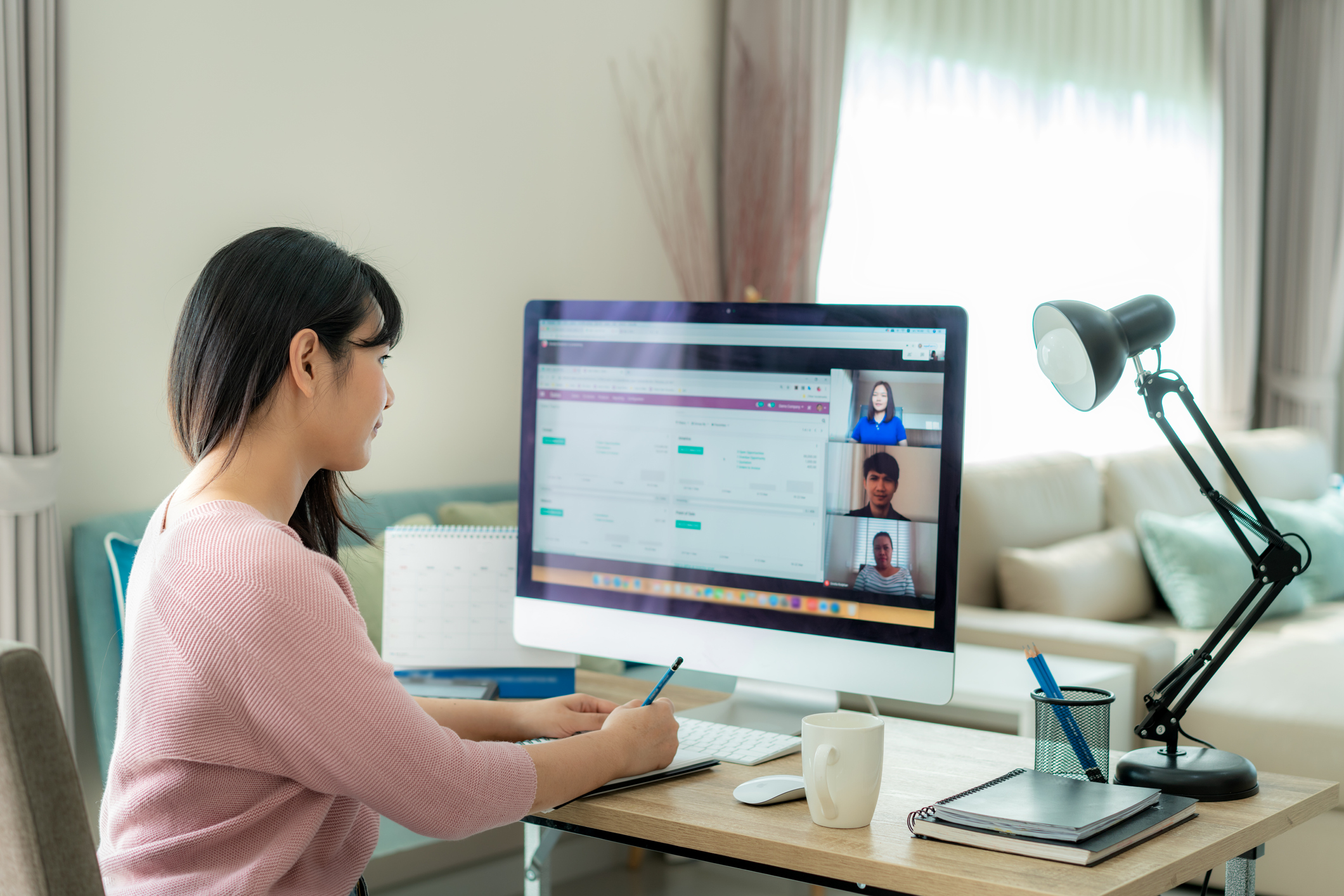 Woman sitting at desk taking notes in front of computer with couch next to her desk