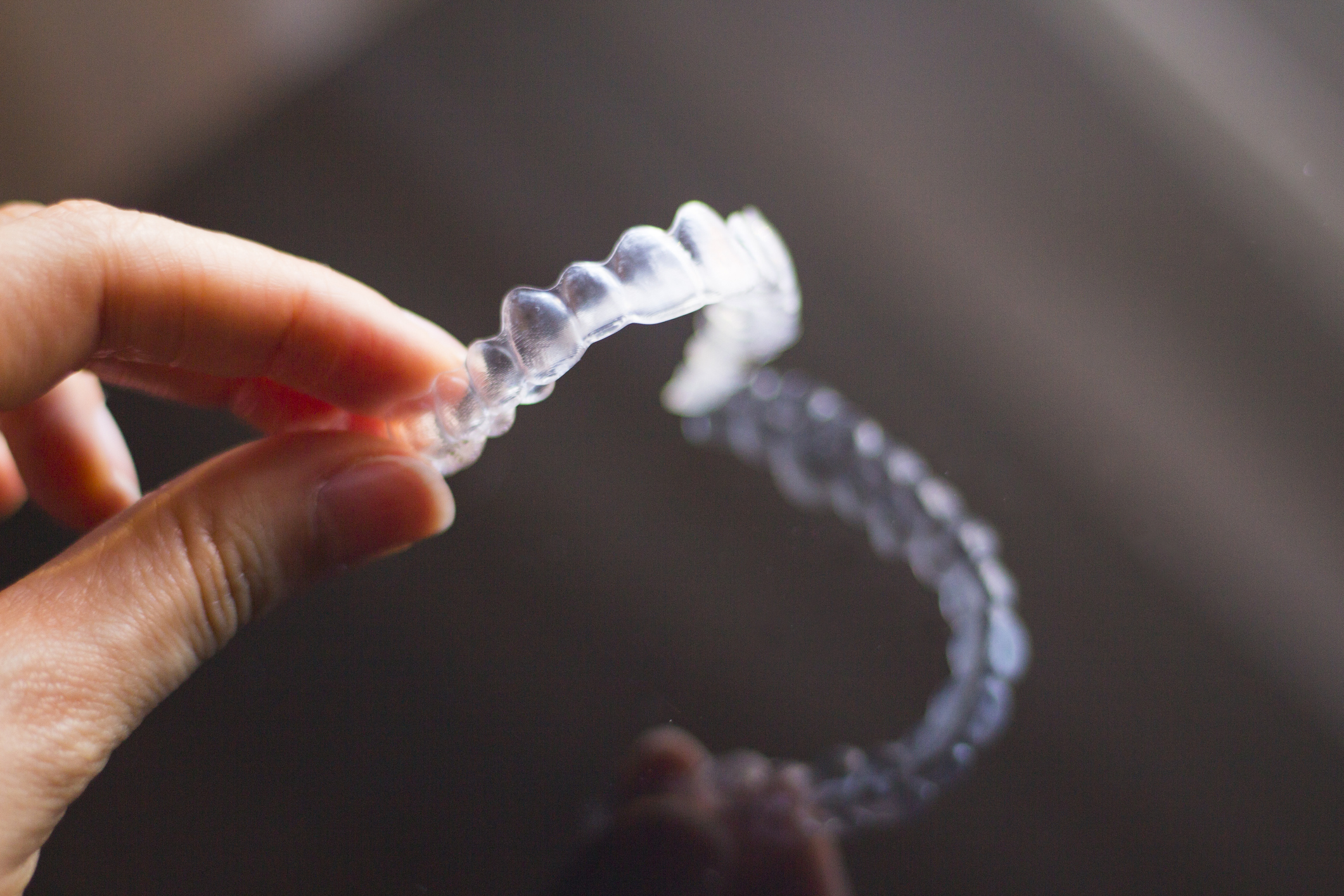 Hand holding clear aligner with reflection appearing on a table surface