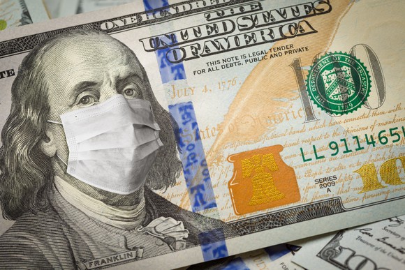 American 100 dollar bill with a face mask over Benjamin Franklin's face.