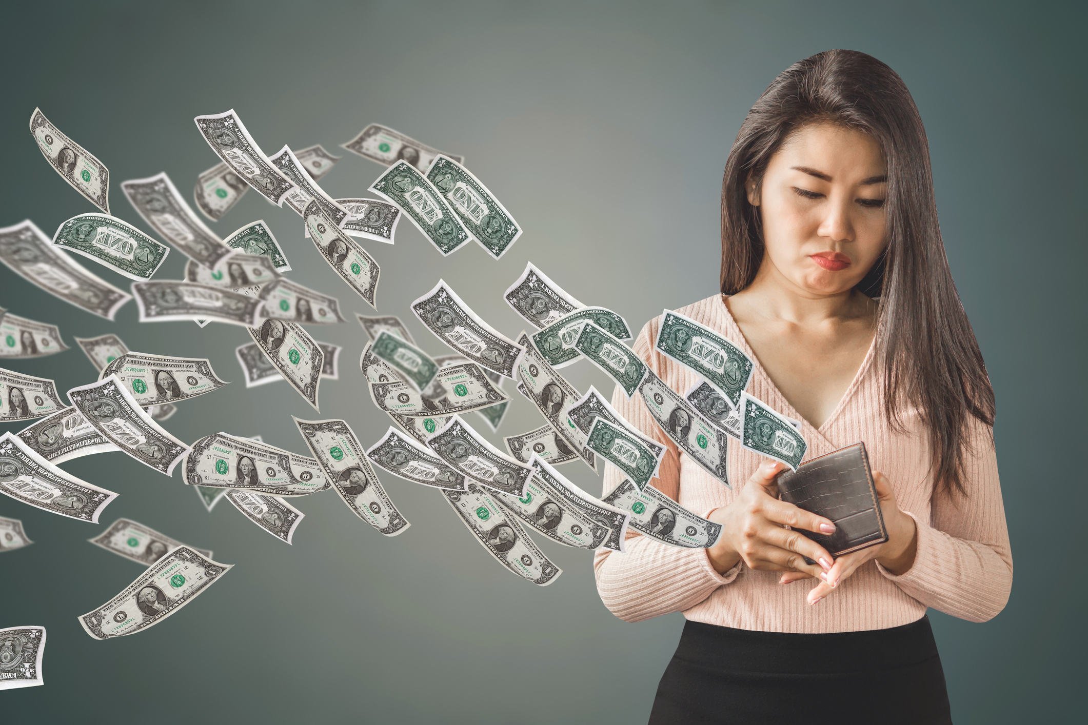 A woman watching dollar bills fly away out of an open wallet.