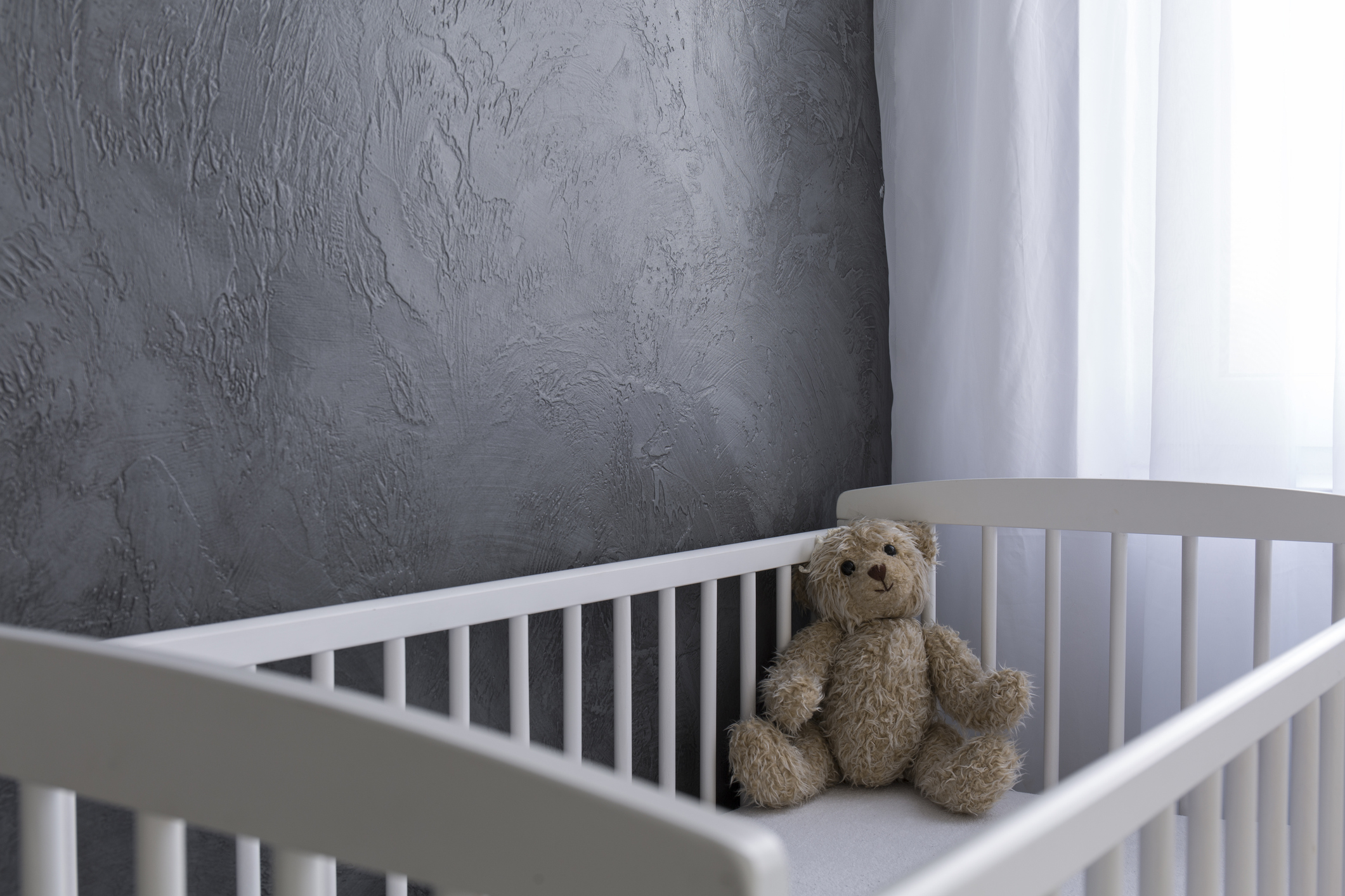 A teddy bear sitting in an otherwise empty crib.