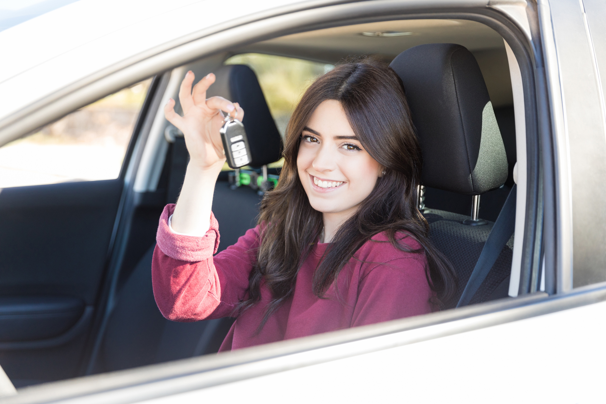 A young woman sits in a car holding up the keys.