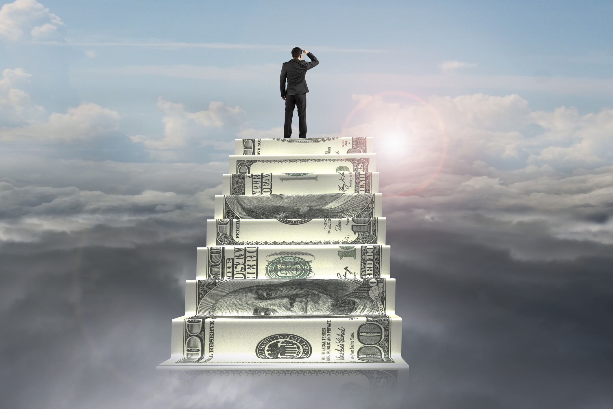 businessman on top of money stairs looking at sunlight